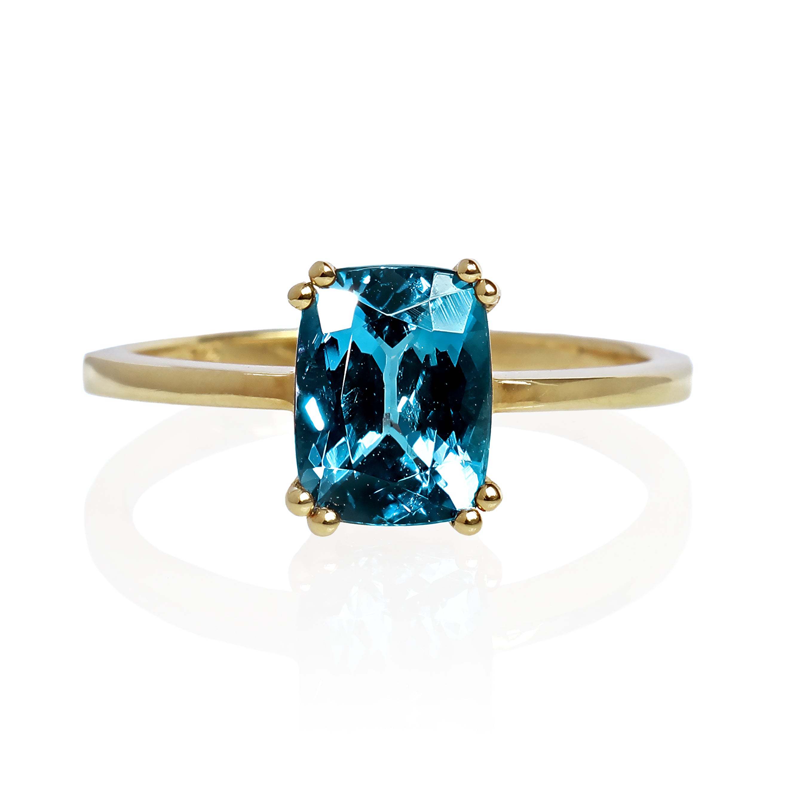 A product photo of a yellow gold london blue topaz ring sitting against a white background. The golden band is plain and smooth, contrasted by the large rectangular cushion-cut ocean blue stone in the centre.