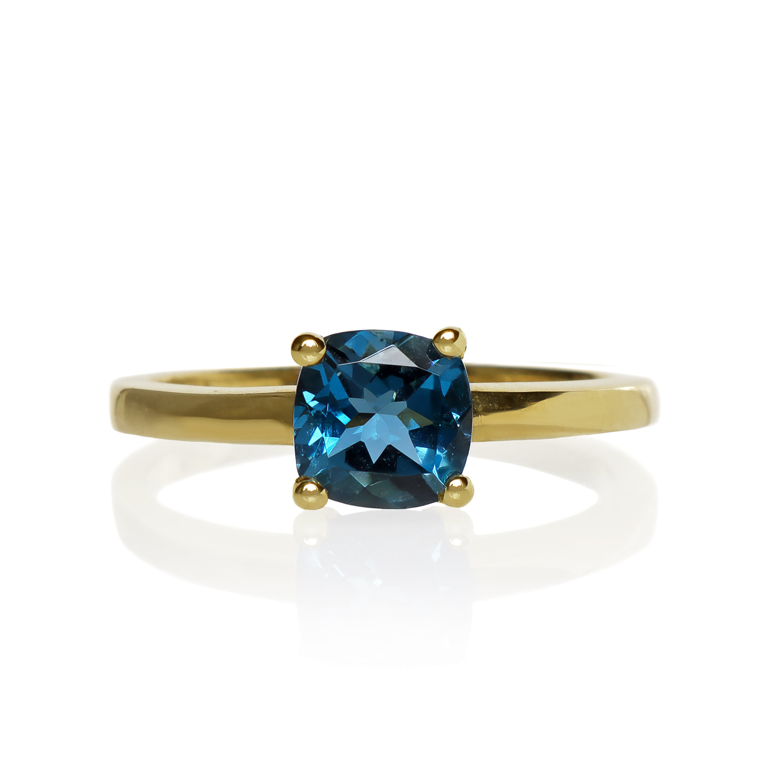 A product photo of a yellow gold london blue topaz ring sitting against a white background. The golden band is plain and smooth, contrasted by the large square cushion-cut ocean blue stone in the centre.