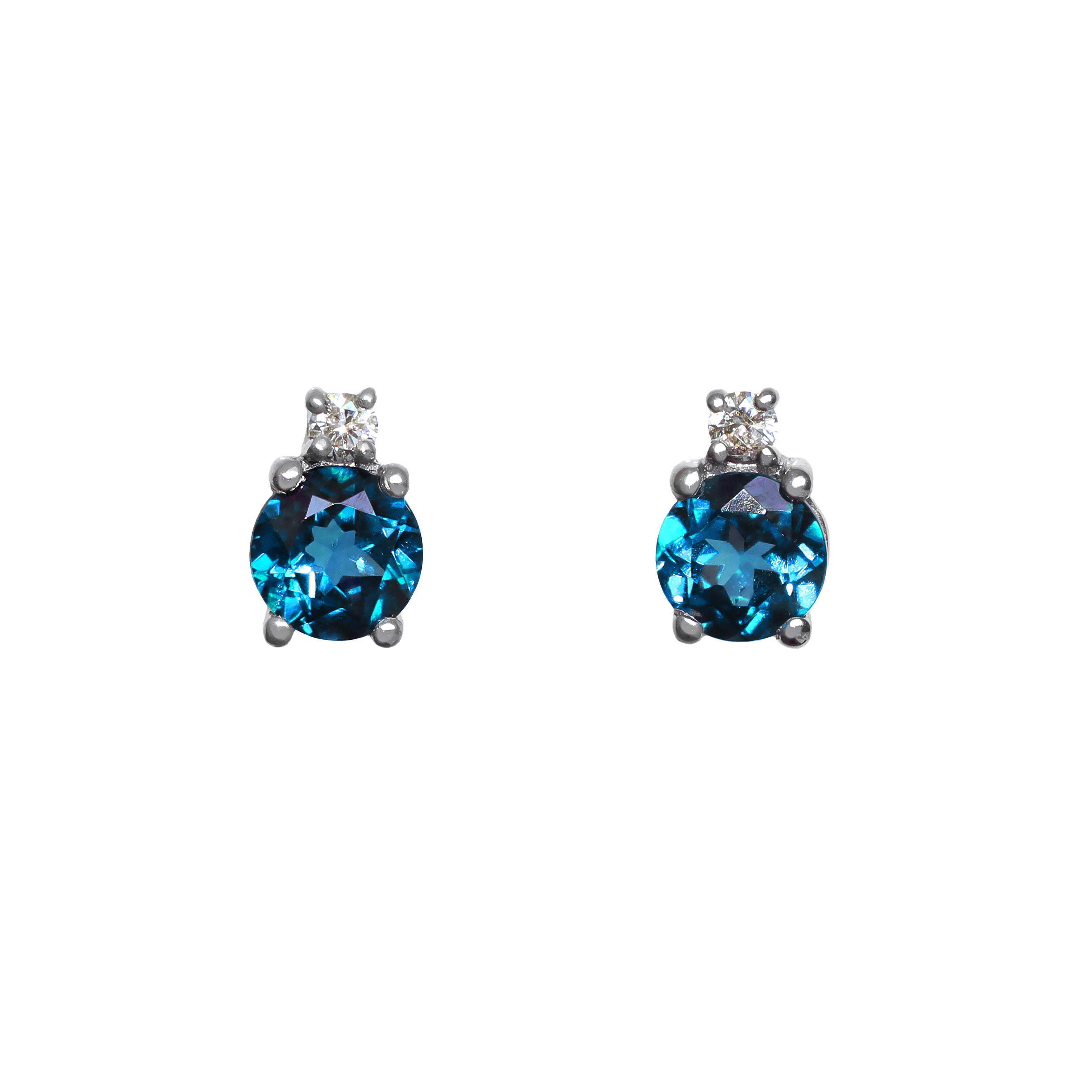 A product photo of a pair of white gold london blue topaz earrings sitting against a white background. The simple circle-cut stones are complimented by a single white diamond atop each stone, encased in white gold.