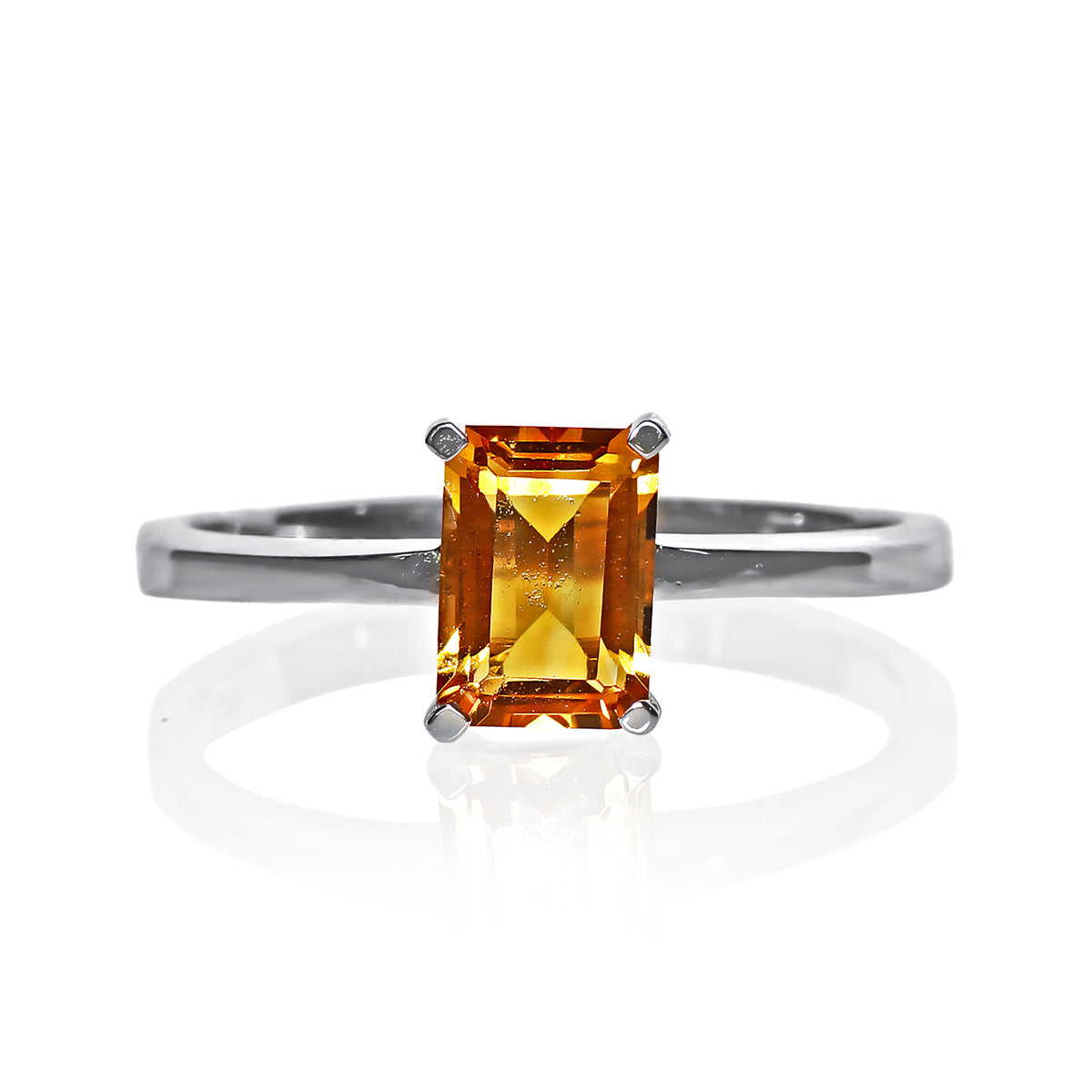 A product photo of a silver ring with an emerald-cut citrine centre stone sitting on a white background. The silver band is simple and smooth, connecting on either side of a vertically-oriented emerald-cut citrine centre stone held in placfe by four silver claws. The citrine jewel is almost honey-coloured, reflecting a warm orangey yellow colour across its multi-faceted surface.