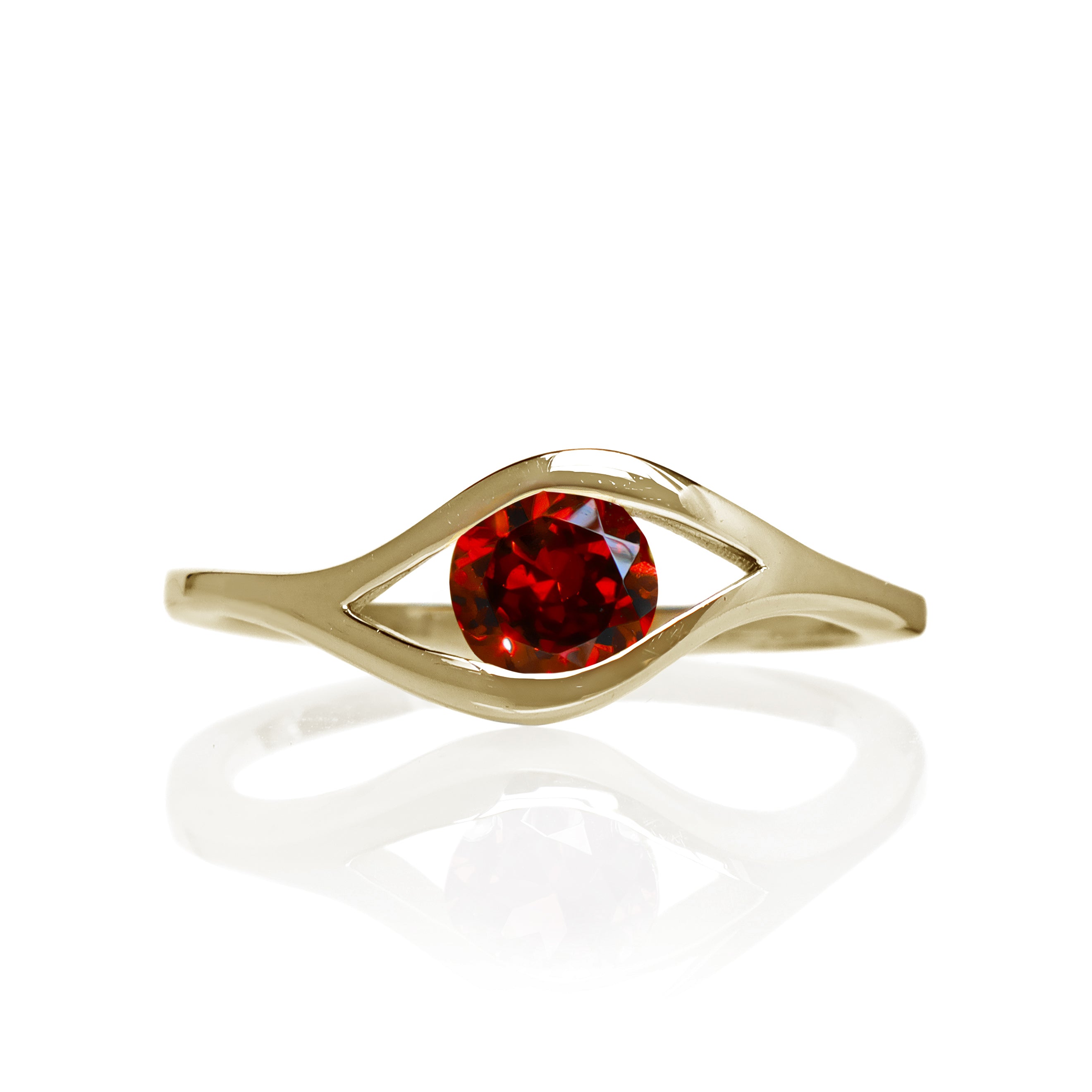 A product photo of a Round Garnet Ring in 9k Yellow Gold sitting on a plain white background. The 5.5mm garnet sits in the centre, and a simple golden band splits on either side of the jewel, meeting above and below, holding it in place like the corners of an eye. The stone is a deep red, reflecting sanguine hues across its multi-faceted edges.