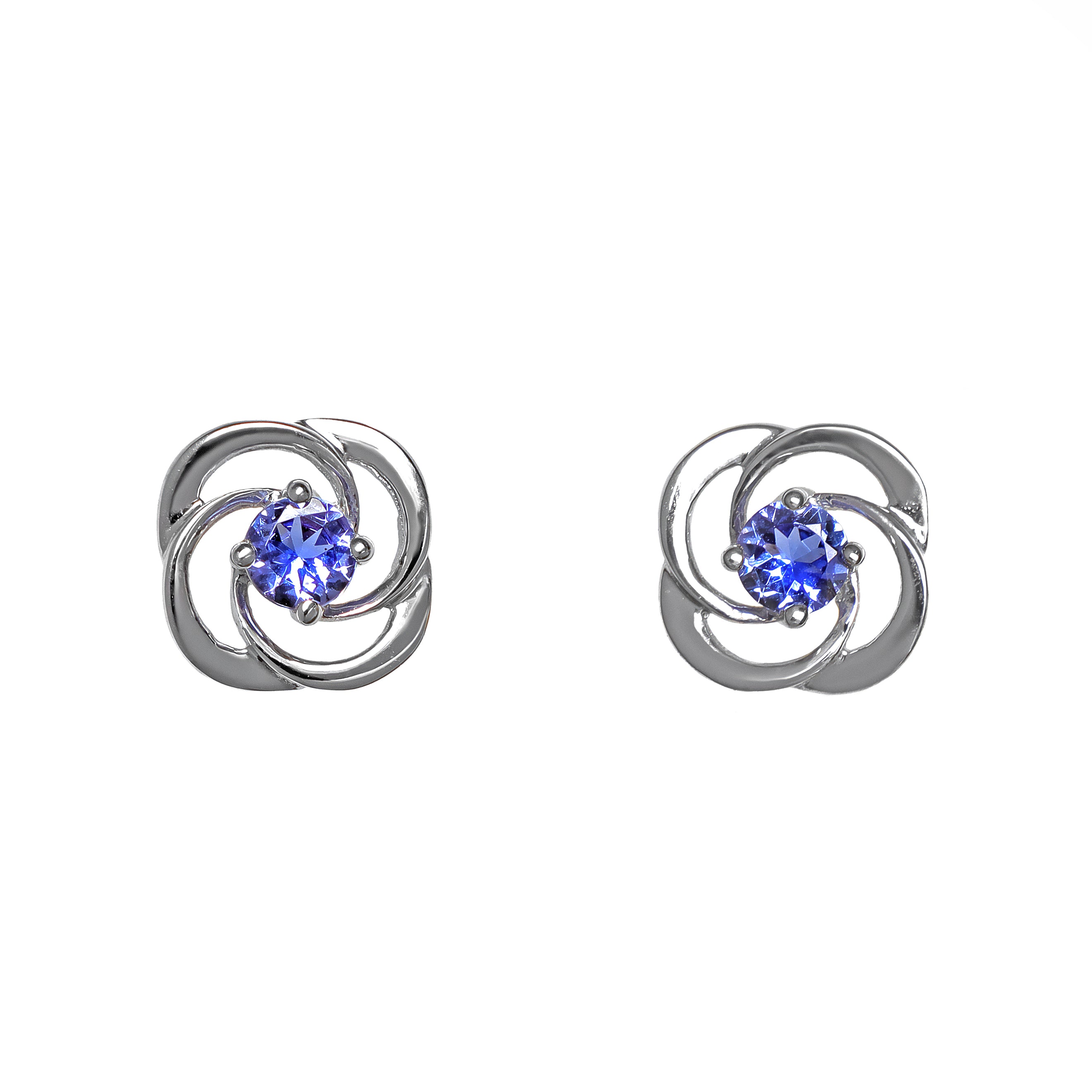 A product photo of white gold stud tanzanite earrings sitting on a white background. The small stones are framed by ornate, flowery white gold backs. The deep blue tanzanite stones reflect violet blue and indigo light from their many edges.