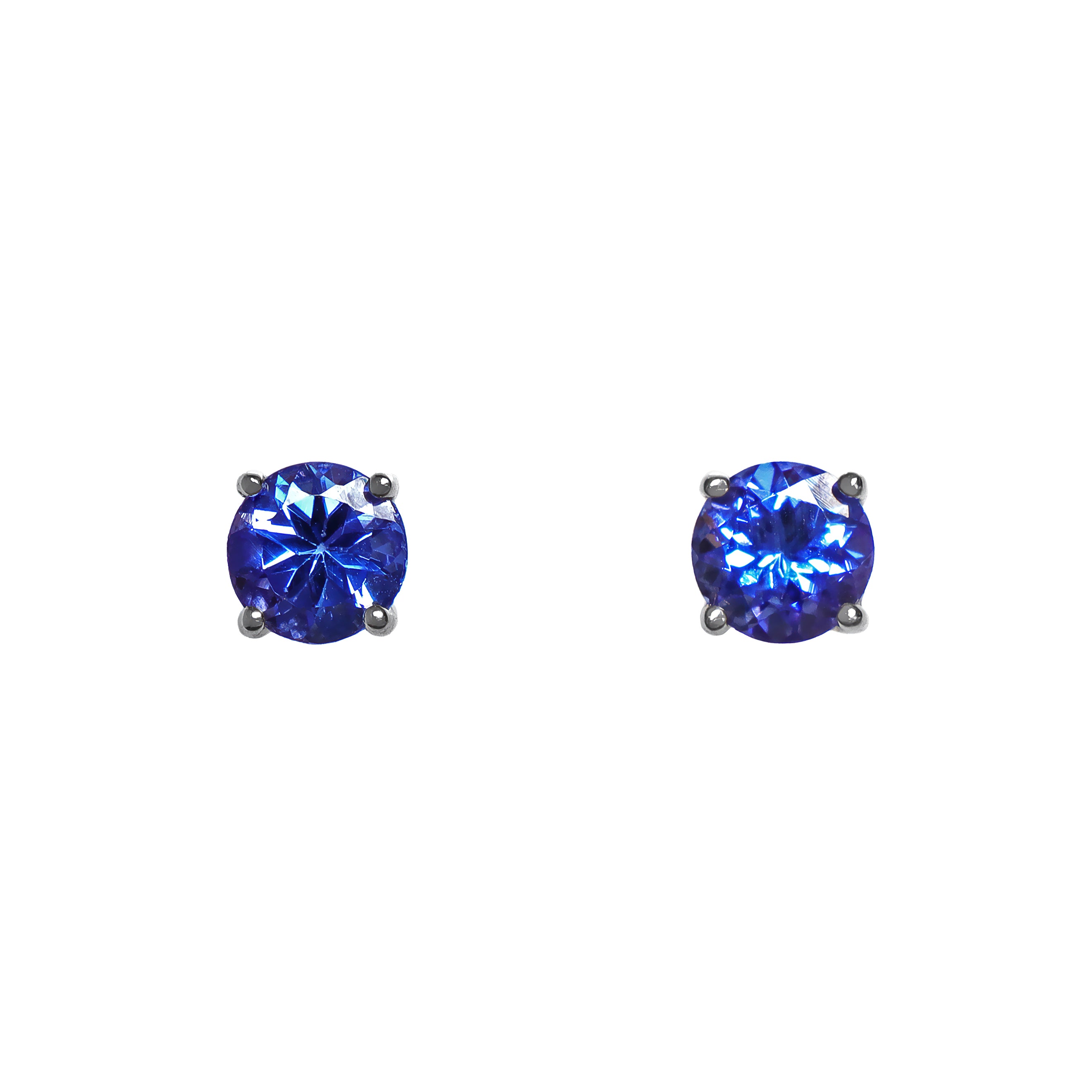 A product photo of white gold tanzanite stud earrings sitting on a white background. The round stones are held in place by 4 claws each, and reflect blue and indigo light from their many edges.