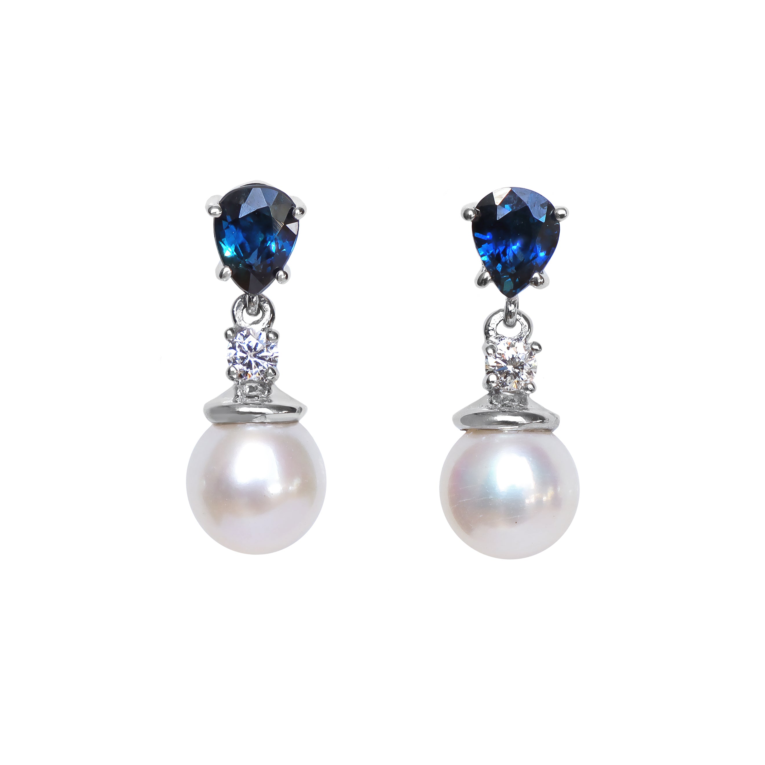 A product photo of a pair of ornate pearl drop stud earrings in white gold suspended over a white background. The pearls are creamy white and round, with one small diamond followed by a pear-shaped sapphire on each piece linking them to the back of the golden stud.