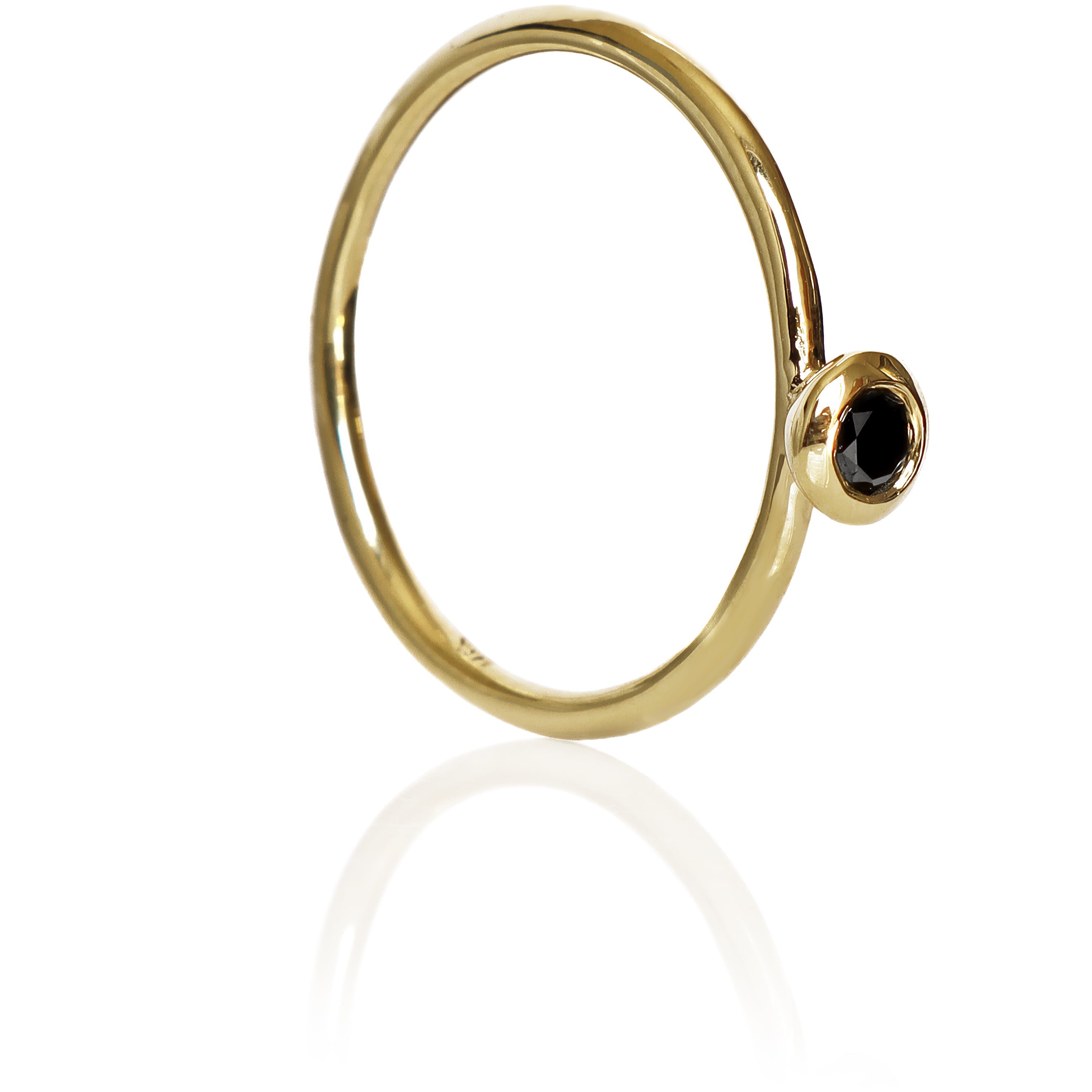 A product photo of a delicate yellow gold stacking ring with a tiny, bezel-set black diamond in the centre sitting on a white background. The band is slim and thread-like, with the focus drawn to the petite 3mm glinting black centre stone.