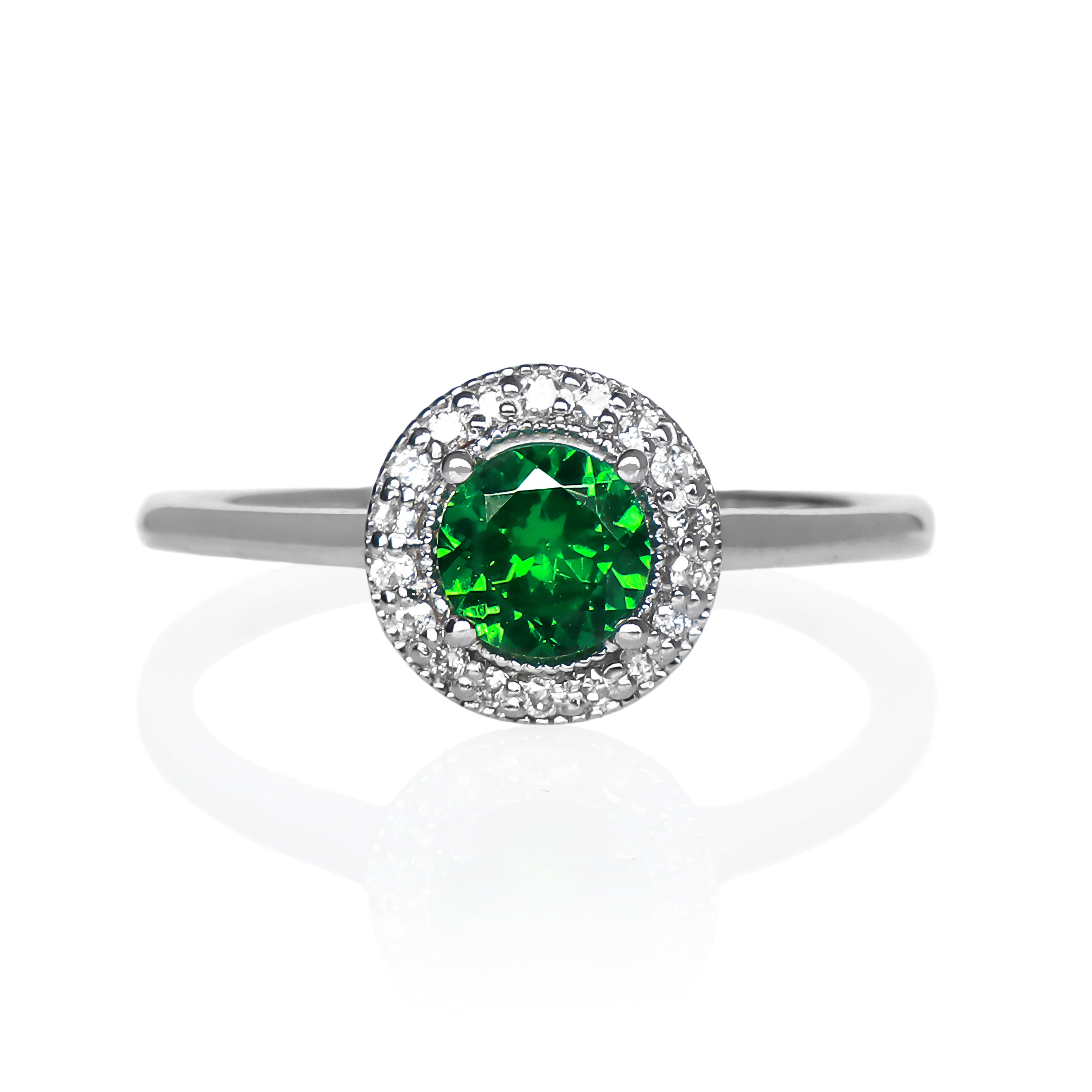 A product photo of a classic diamond halo tsavorite ring in solid 9k white gold on a white background. The diamond halo is framed by a thick band of solid 9k white gold, and the rounded band is smooth and minimalistic. The deep, verdant-green tsavorite centre stone is held in place by 4 claws and reflects light off of its many facets. The green gemstone colour would be a good emerald substitute.