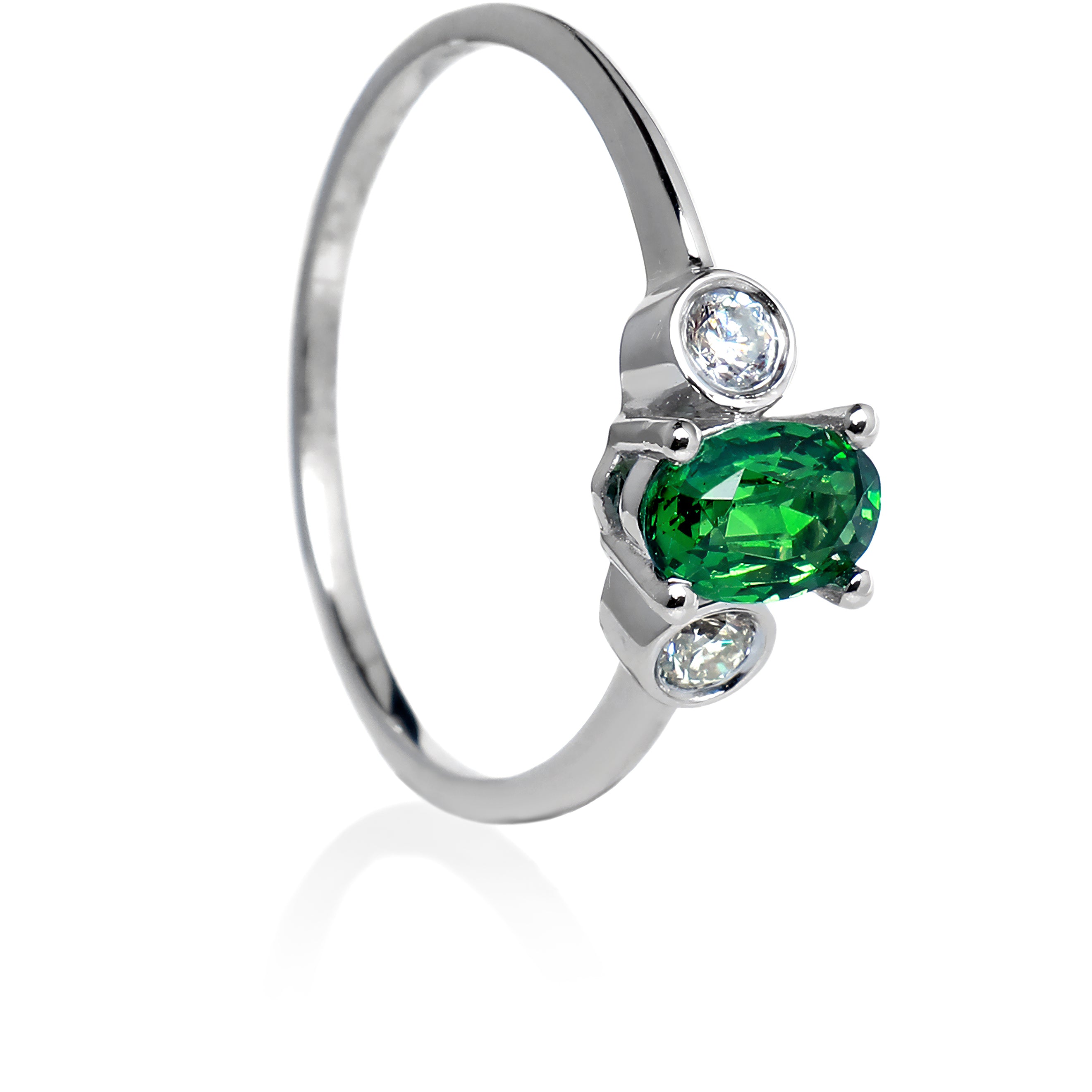 A product photo of a uniquely elegant tsavorite and duo diamond ring in solid 9k white gold on a white background. The deep, verdant-green tsavorite centre stone is held in place by 4 claws and reflects light off of its many facets, while the bezel-set diamonds are framed by a solid layer of white gold. The green gemstone colour would be a good emerald substitute.
