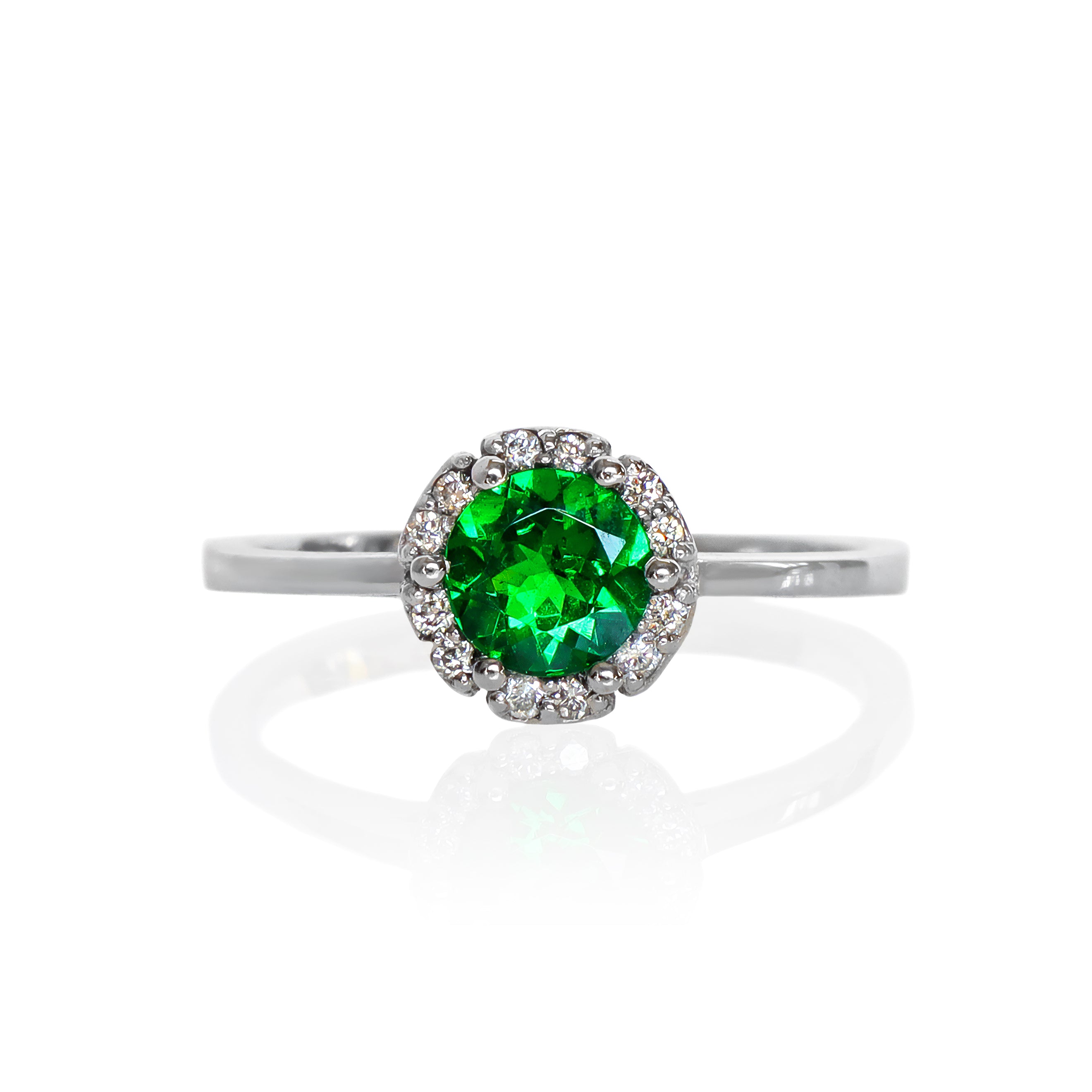 A product photo of a classic diamond halo tsavorite ring in solid 9k white gold on a white background. The rounded band is smooth and minimalistic. The deep, verdant-green tsavorite centre stone is held in place by 6 claws and reflects light off of its many facets. The green gemstone colour be a good emerald substitute.