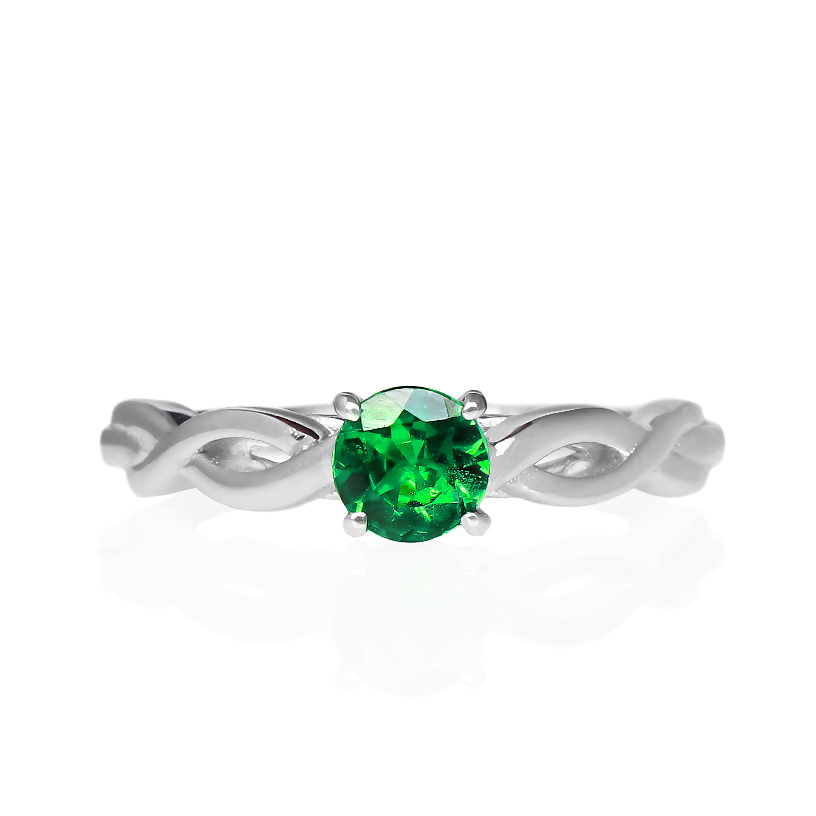 A product photo of an ornate white gold ring with a tsavorite centre stone sitting on a white background. The band splits halfway along its length, becoming twisting and serpentine in appearance before meeting on either side of the deep 5mm round tsavorite, which is held in place by 4 silver claws. The green gemstone colour be a good emerald substitute.