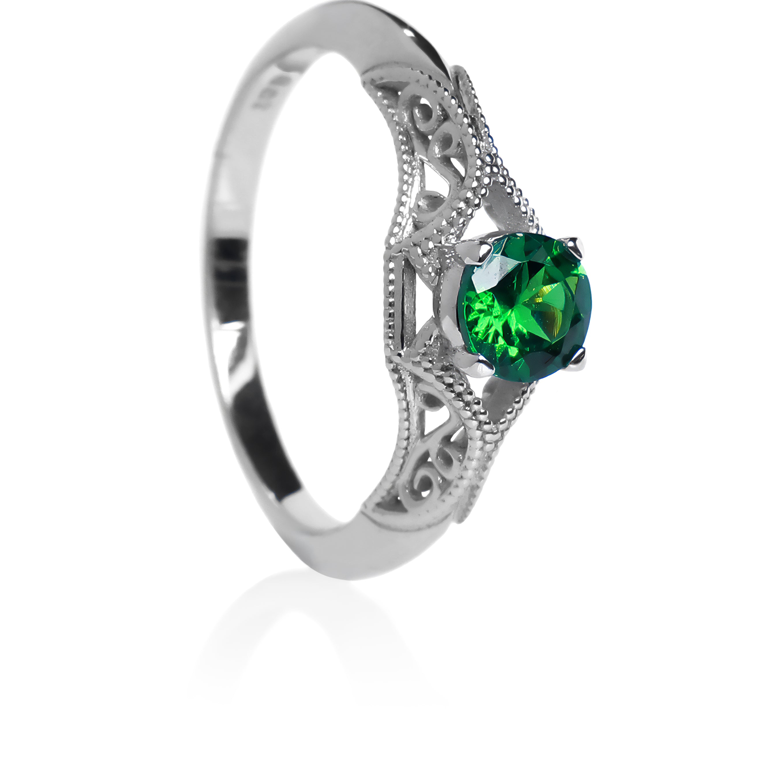 A product photo of an ornate, filigree-detailed white gold ring - reminiscent of an elvish fantasy ring with a deep forest green tsavorite centre stone. The band is detailed with delicate curves and patterns for about half of its length around the dazzling tsavorite stone, before smoothing out towards the back of the ring. The green gemstone colour would be a good emerald substitute.