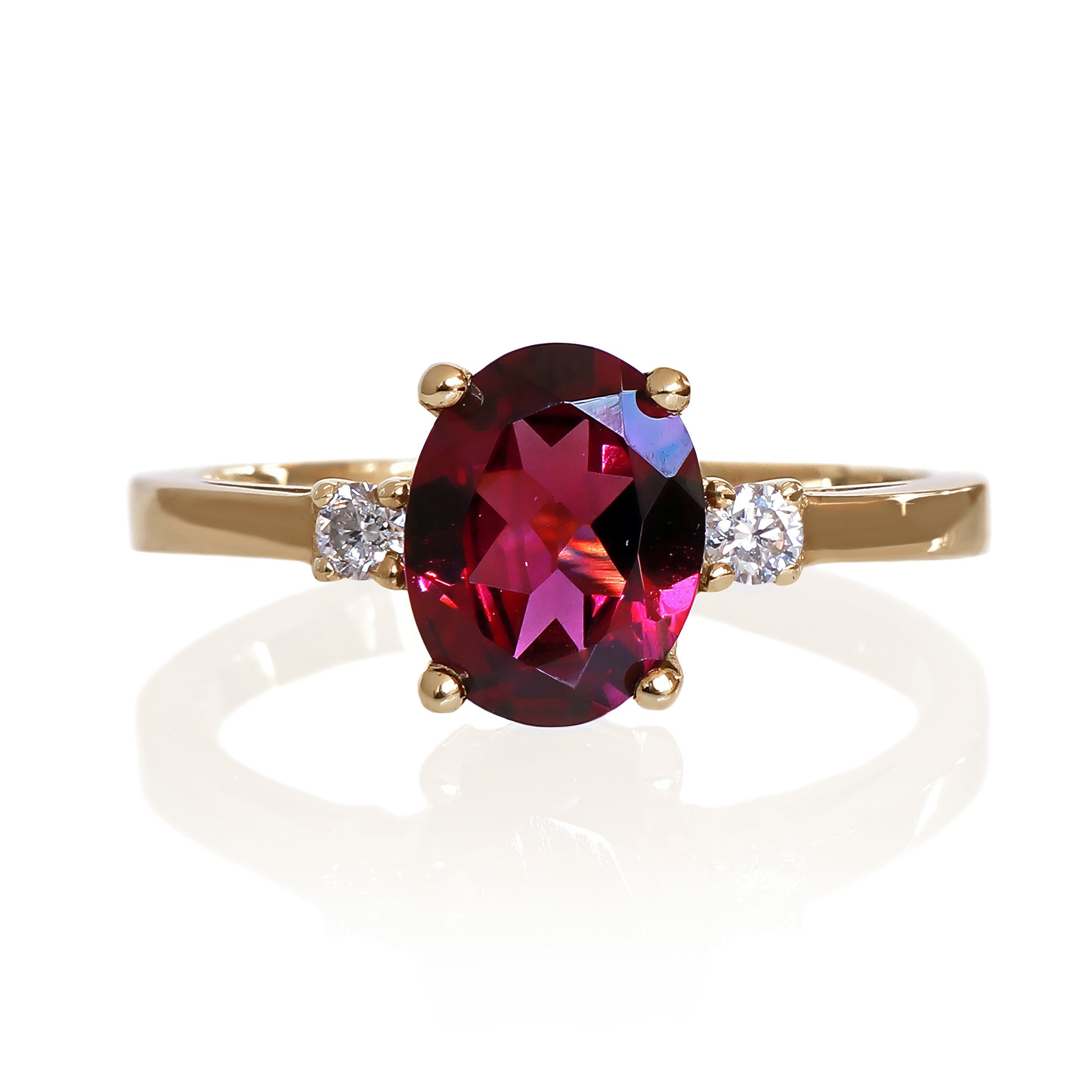 A product photo of a dainty and elegant yellow gold ring with a stunning trio of rhodalite and diamonds sitting against a white background. The largest of the stones sits in the centre, an oval rhodalite - hugged by two smaller circular white diamonds on either side.