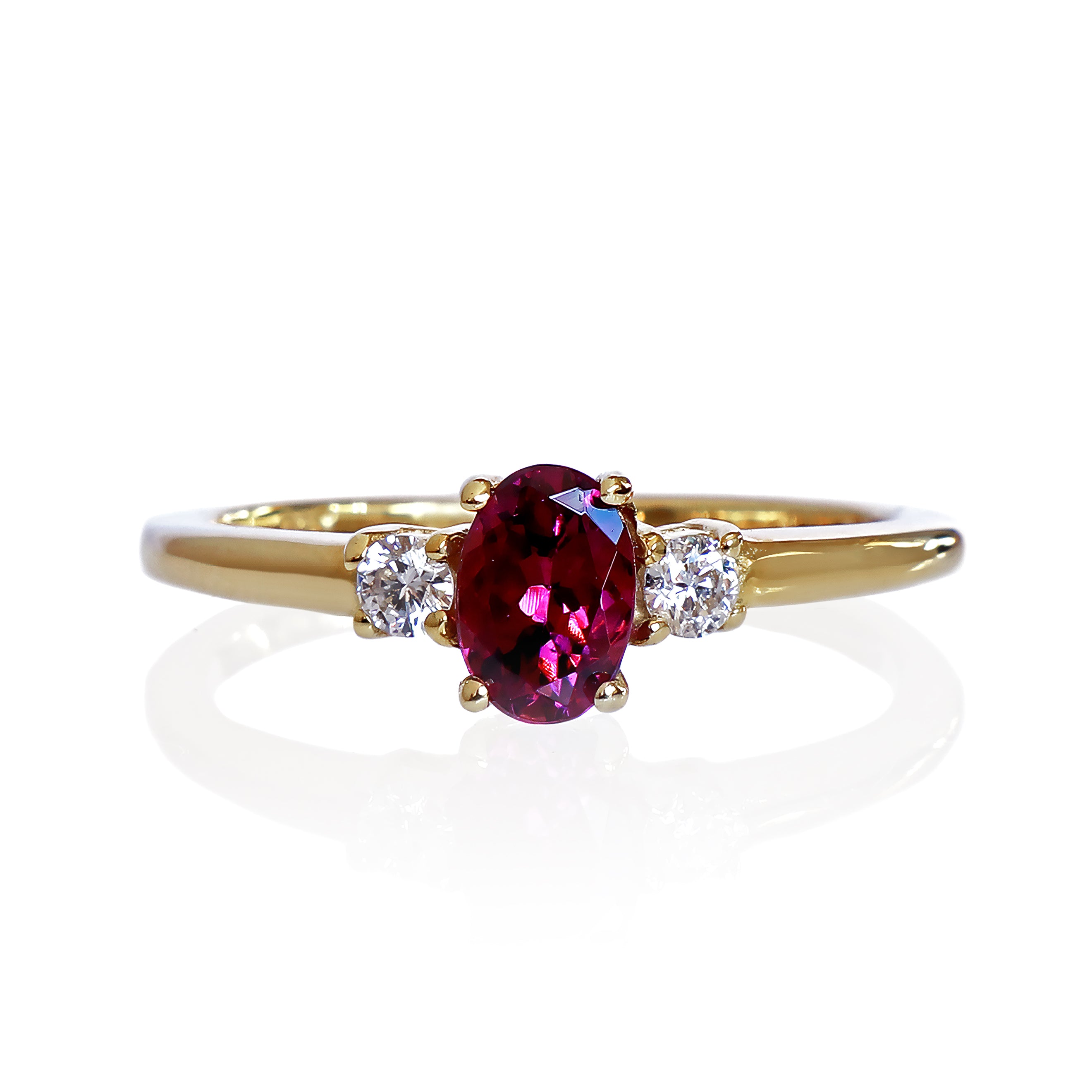A product photo of a yellow gold rhodalite and diamond trio ring sitting on a white background. The 6x4mm oval purple rhodalite gemstone stands in stark contrast to the 0.03ct white diamond stones on either side.