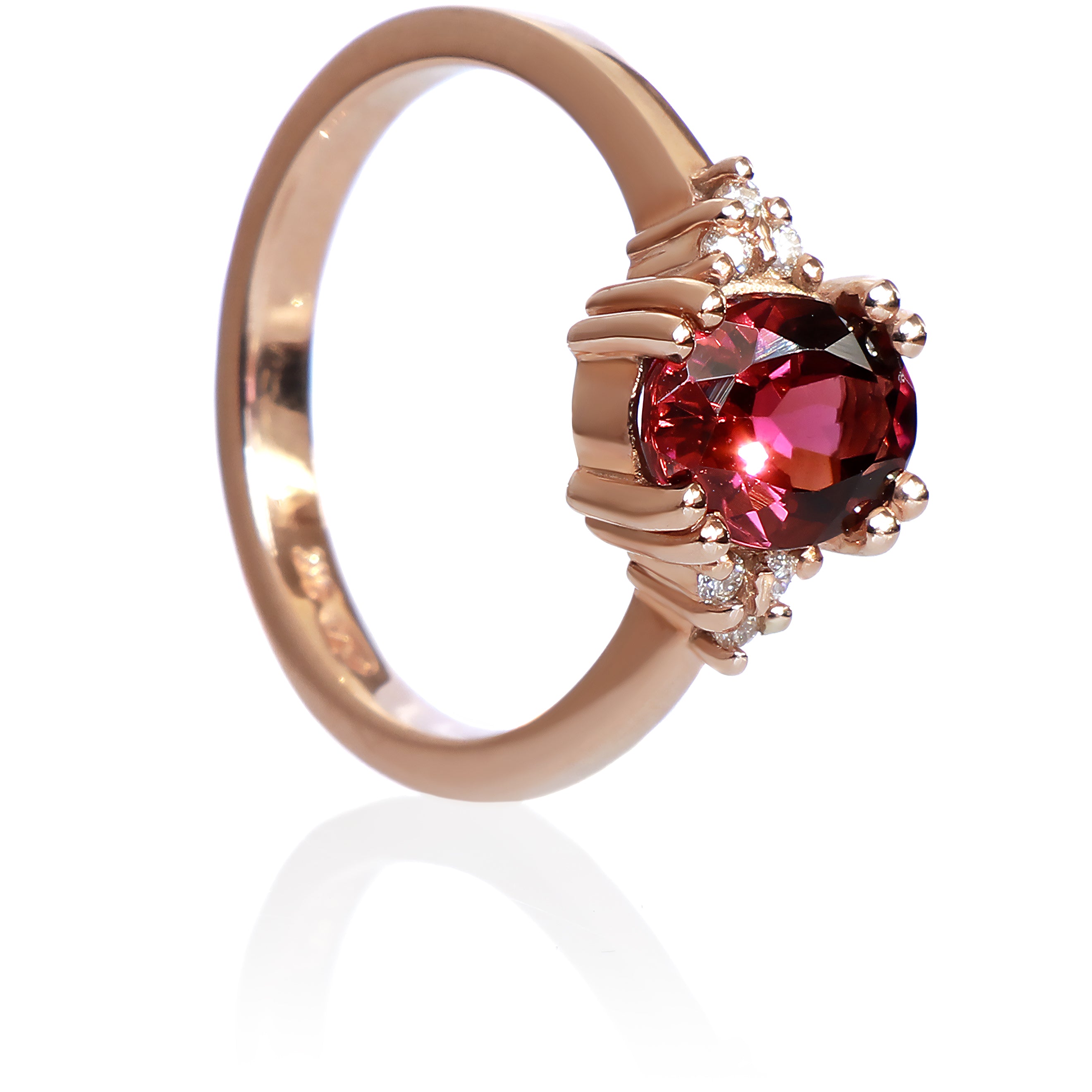A product photo of a rose gold rhodalite and diamond trio ring sitting on a white background. The oval purple rhodalite gemstone stands in stark contrast to the little clusters of three white diamond stones on either side.