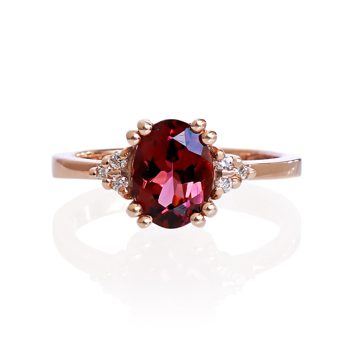 A product photo of a rose gold rhodalite and diamond trio ring sitting on a white background. The oval purple rhodalite gemstone stands in stark contrast to the little clusters of three white diamond stones on either side.