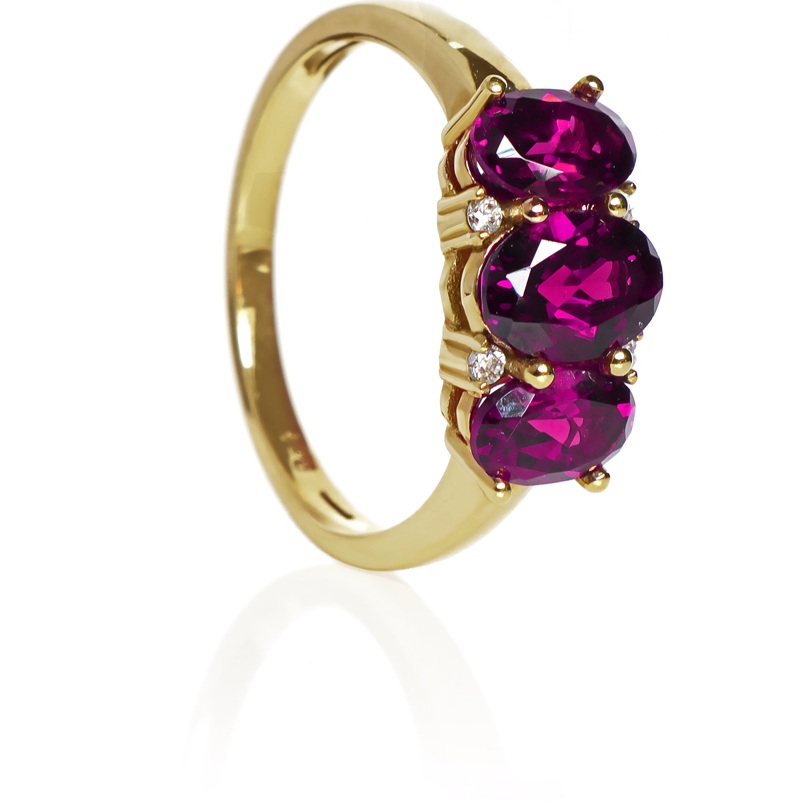 A product photo of a Grape Garnet Trio & Diamond Ring in Yellow Gold sitting on a plain white background. The largest garnet centre stone measures 7x5mm, with 4 tiny diamonds nestled against it, two on each side. The grape garnet stones are deep and warm, reflecting magenta hues across their multi-faceted edges.