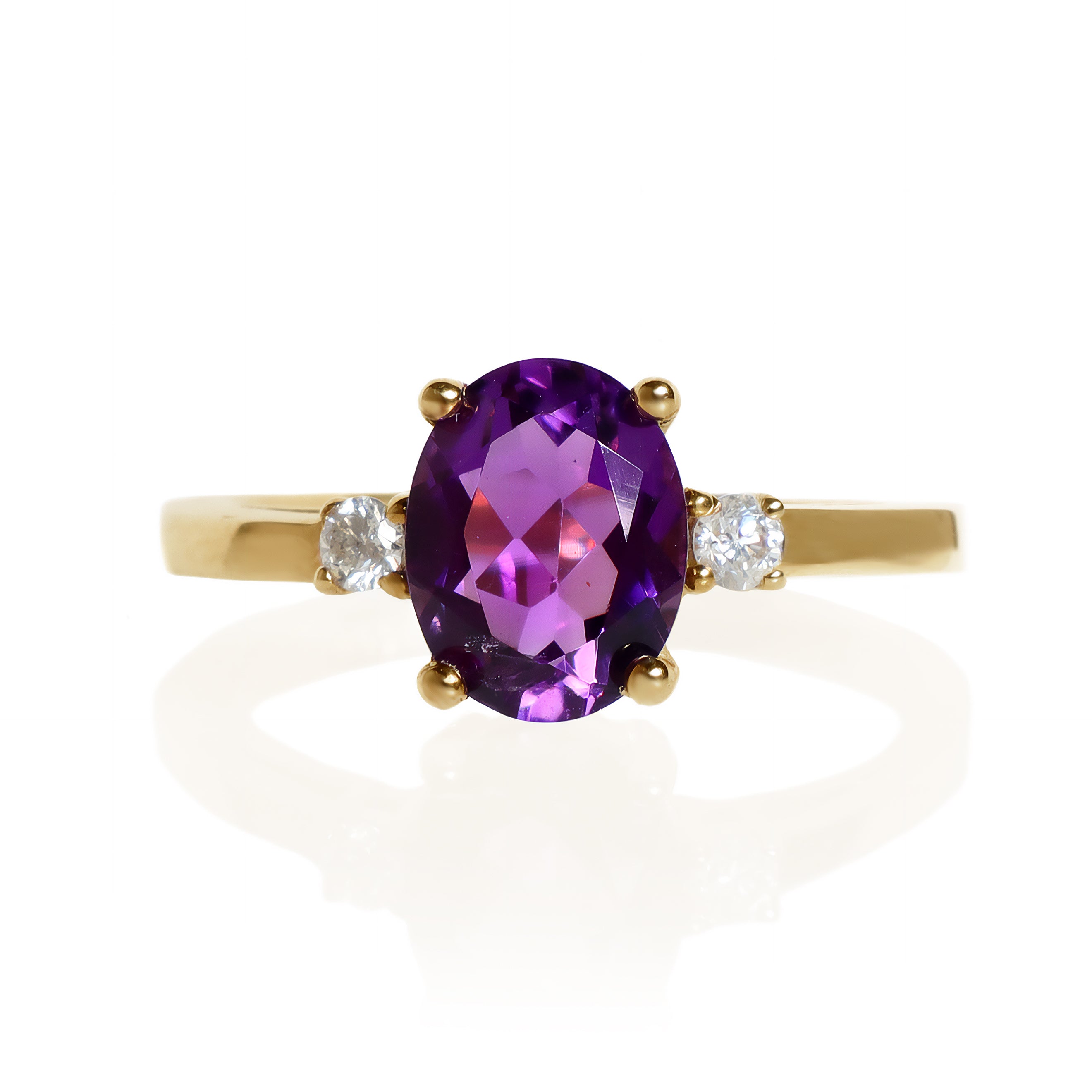A product photo of a dainty and elegant yellow gold ring with a stunning trio of amethyst and diamonds sitting against a white background. The largest of the stones sits in the centre, an oval amethyst - hugged by two smaller circular white diamonds on either side.