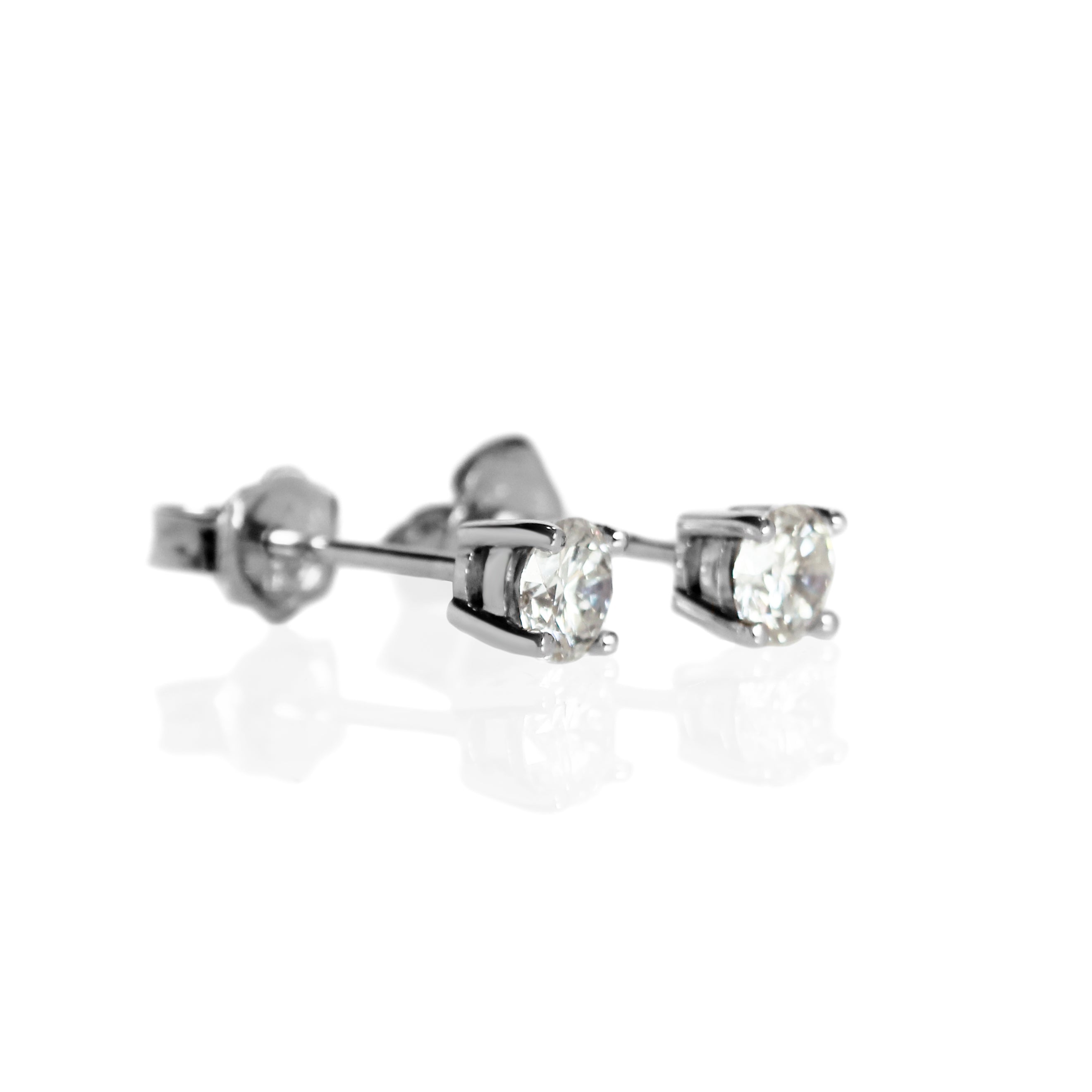 A product photo of a pair of 9 karat white gold lab diamond stud earrings sitting in the sun on a white textured background. The brilliant, colourless half pointer round diamonds measure approximately 4mm across, and are held in place by a simple 4-claw setting.