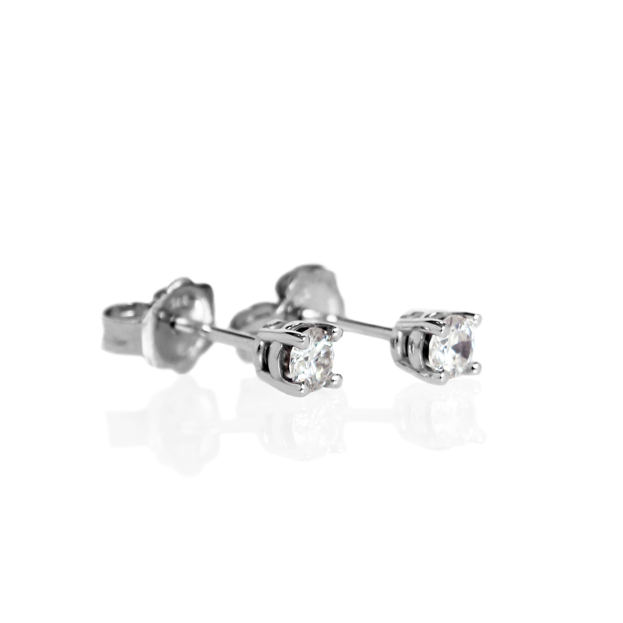 A product photo of a pair of 9 karat white gold lab diamond stud earrings sitting in the sun on a white textured background. The brilliant, colourless half pointer round diamonds measure approximately 3mm across, and are held in place by a simple 4-claw setting.