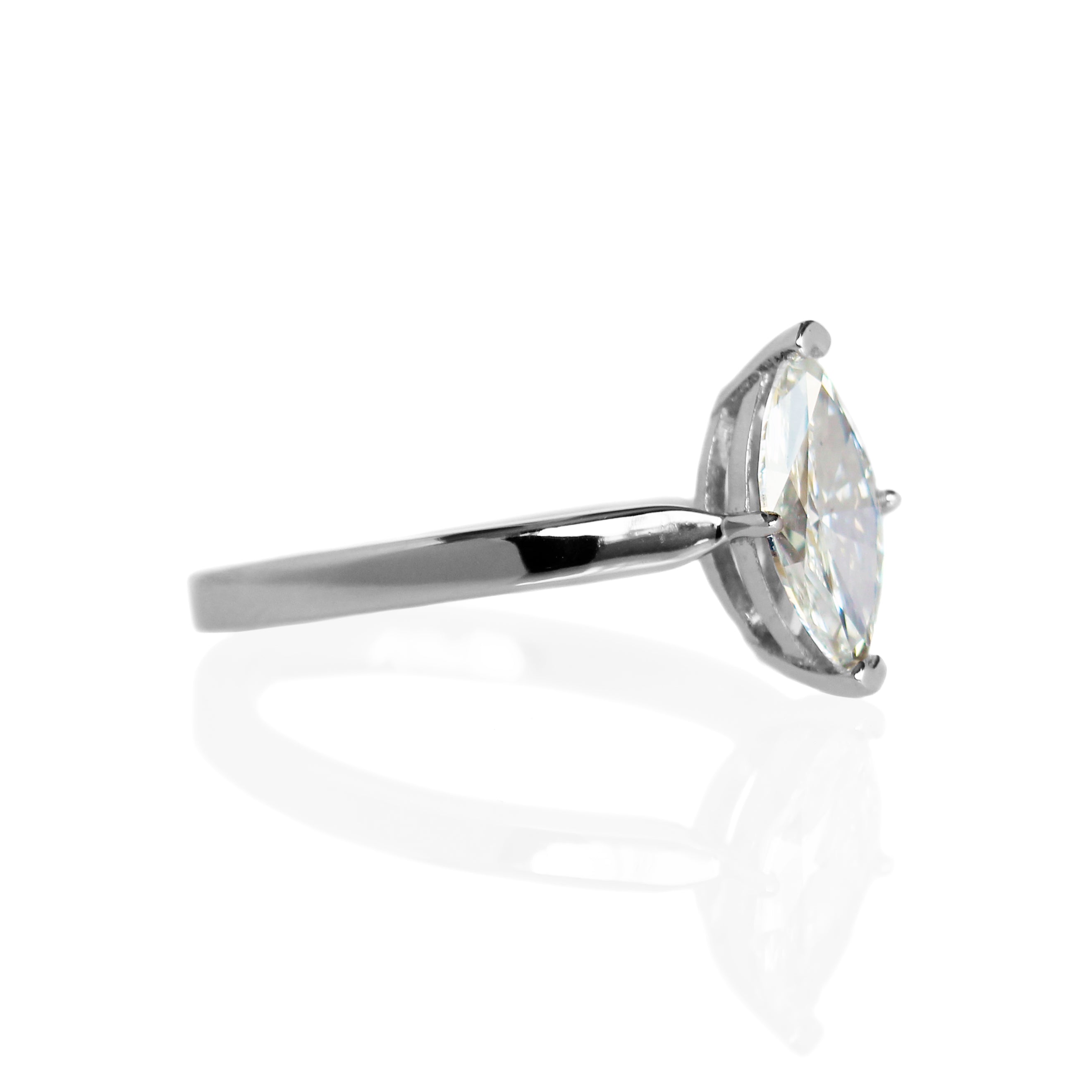 A product photo of a 14 karat white gold lab diamond solitaire engagement ring sitting in the sun on a white textured background. The brilliant, colourless 0.70ct marquise diamond measures about 8.5mm lengthwise, and is held in place by 4 delicate claws in a low-profile prong setting in the middle of a sharply tapered band.