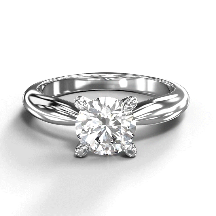 A turntable video of a 14 karat white gold lab diamond solitaire engagement ring sitting in the sun on a white textured background. The brilliant 1 carat round-cut diamond measures 6.3mm lengthwise, and is held in place by 4 delicate claws in a prong setting in the middle of the thickest part of the gold band.