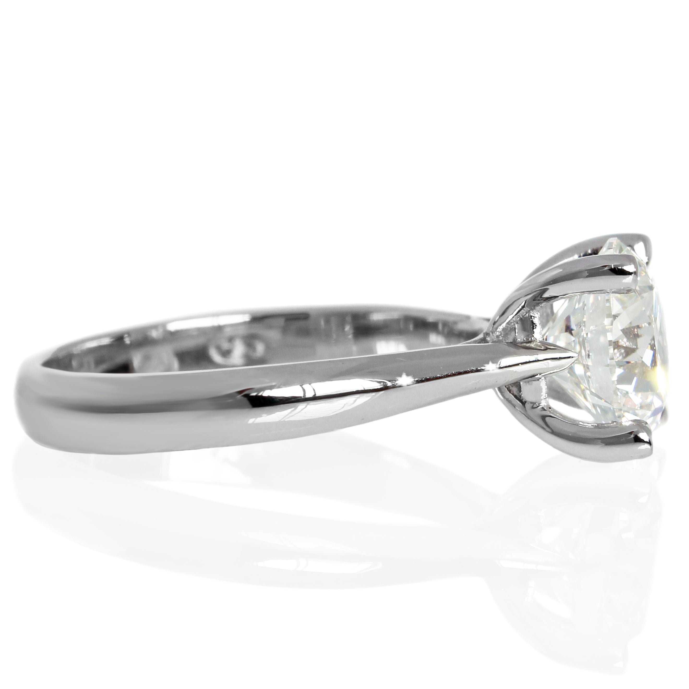 A product photo of a 14 karat white gold lab diamond solitaire engagement ring sitting in the sun on a white textured background. The brilliant, colourless 2 carat round-cut diamond measures over 8mm across, and is held in place by 4 delicate claws in a high-profile cathedral setting in the middle of the thick, tapered band.