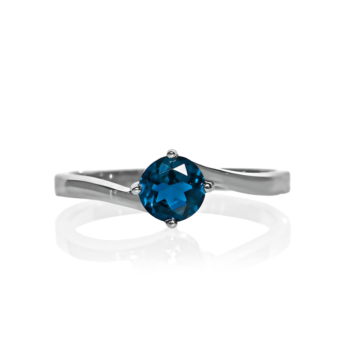 A product photo of a curved-band silver solitaire ring with an ocean blue London Blue Topaz centre stone sitting on a white background. The deep blue gemstone colour would be a good sapphire substitute.