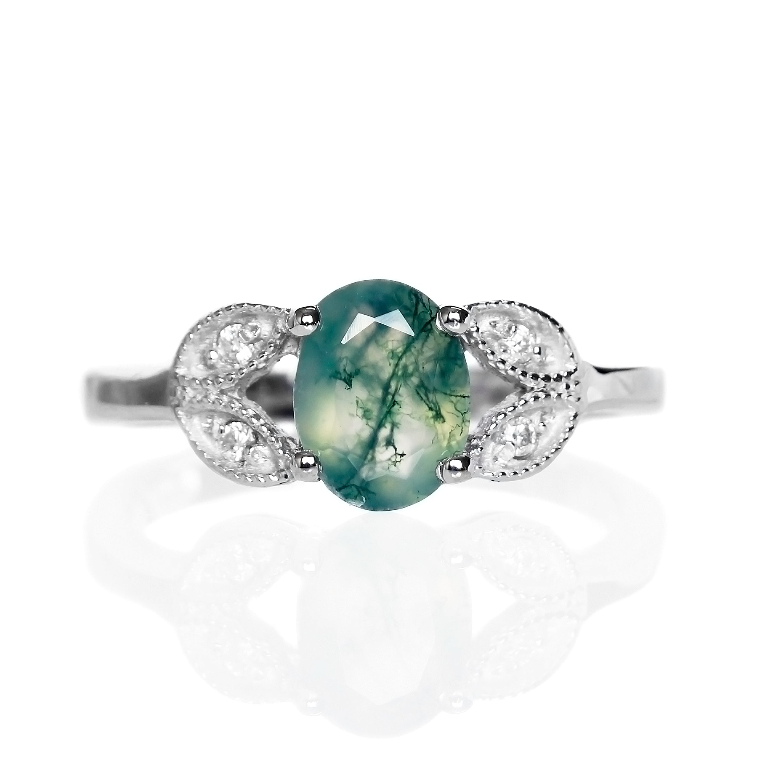 A product photo of an oval moss agate and moissanite ring with floral silver detailing set in solid 925 sterling silver metal. The bold 8x6mm moss agate gemstone is held in place by two petal shapes in filigree silver detailing on either side, each "petal" adorned with a single moissanite in the centre, to a total of 4.
