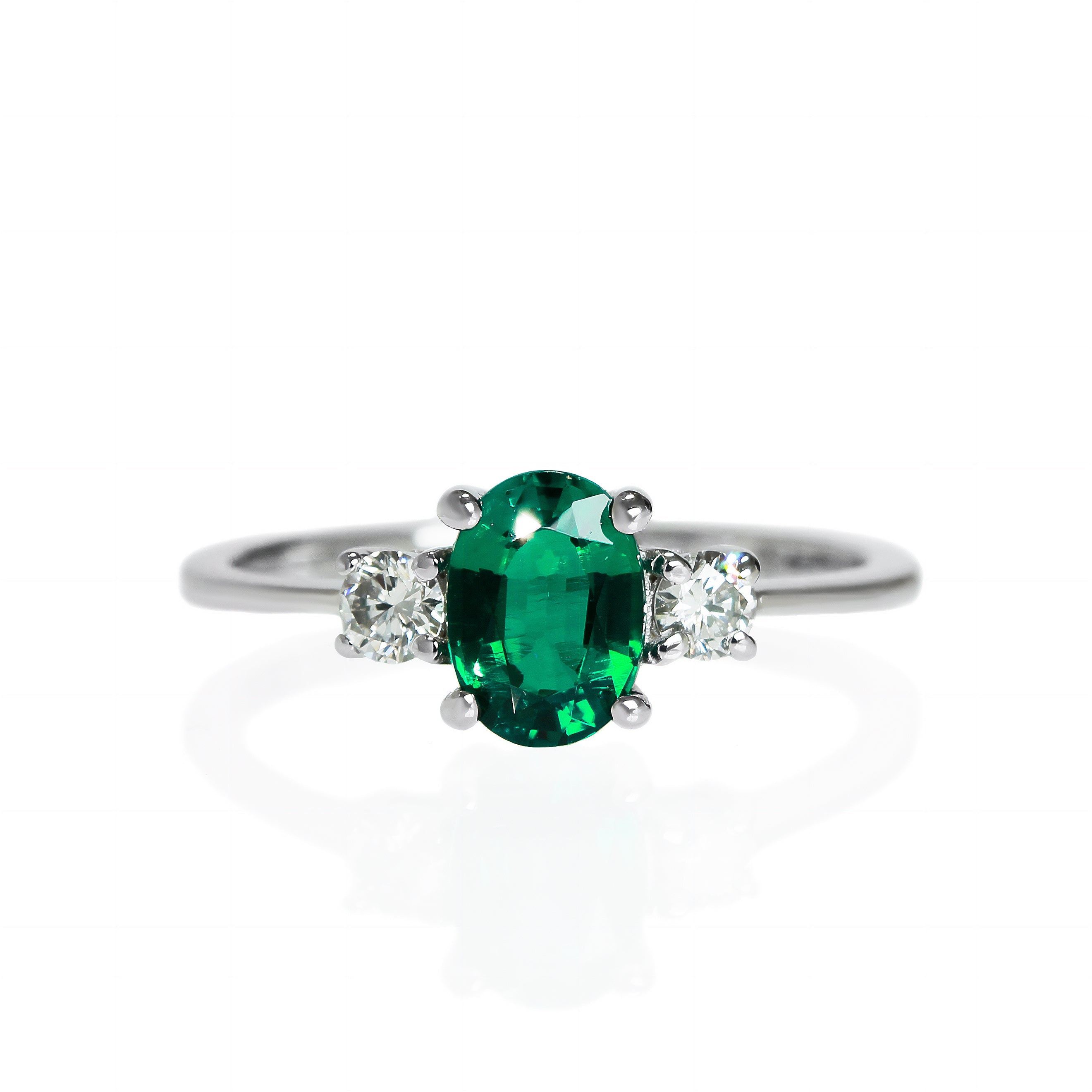 A product photo of a faceted lab emerald and lab diamond ring in 9 karat white gold on a white background. The faceted cut of the lab-grown emerald allows for its sparkling eyeclear appearance to shine, while the round faceted lab diamonds add a burst of sparkling fire to the ring.