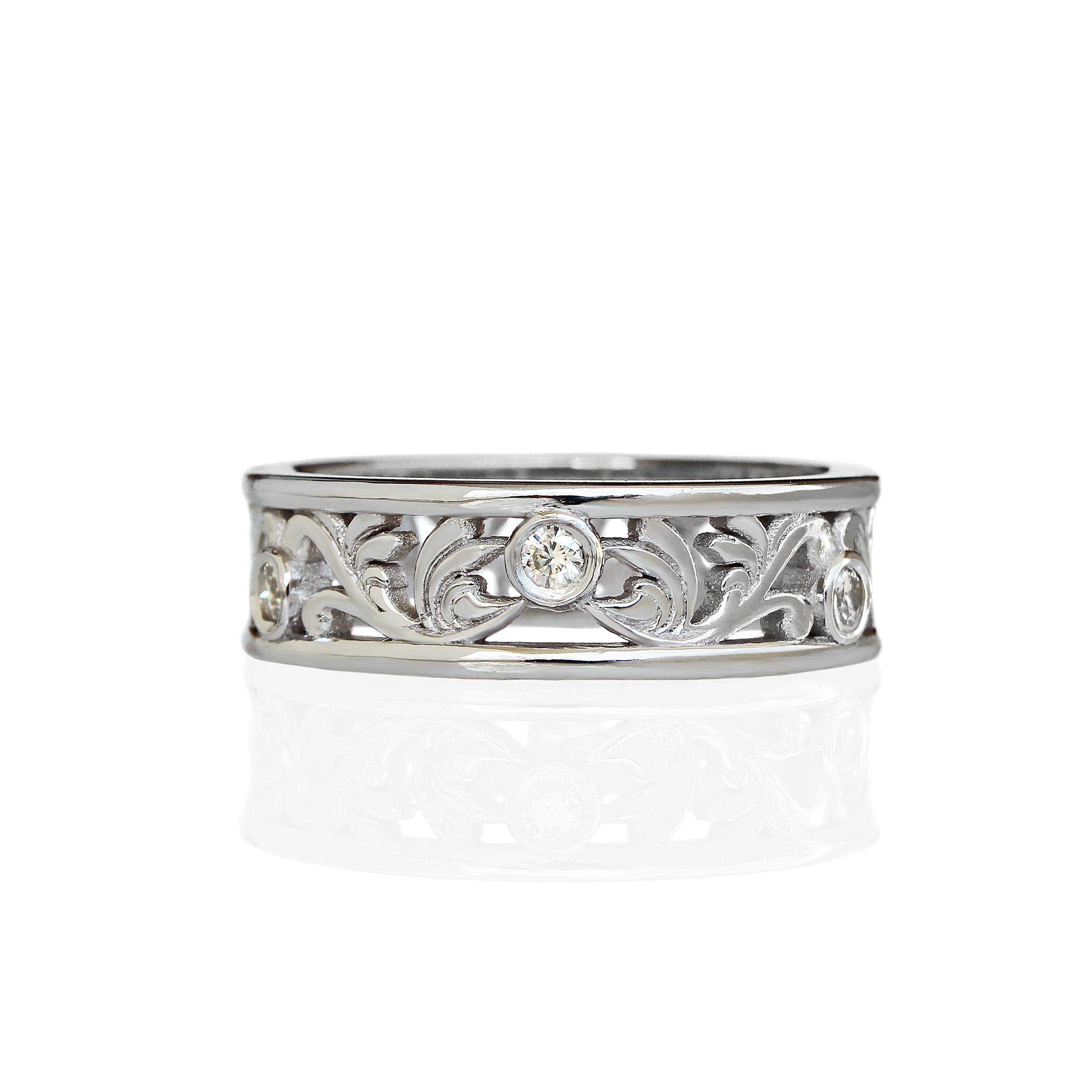 A product photo of a filigree detailed unisex wedding band in solid 925 sterling silver on a white background. The filigree patterning is swirling and floral, reminiscent of a baroque wallpaper, and is punctuated by 6 total 0.03ct dazzling white moissanite gemstones worked into the filigree detailing, each held in place by a bezel setting.