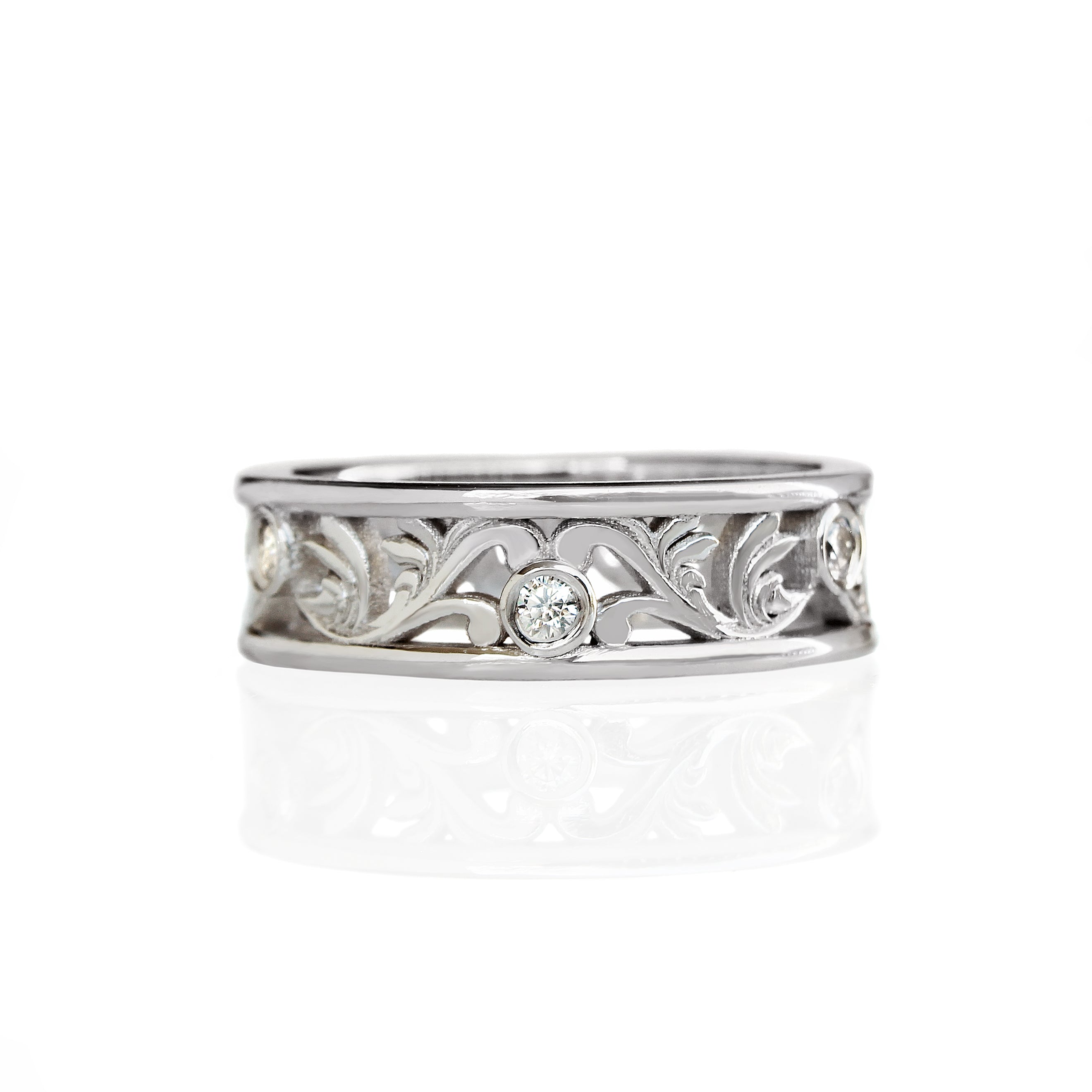 A product photo of a filigree detailed unisex wedding band in solid 925 sterling silver on a white background. The filigree patterning is swirling and floral, reminiscent of a baroque wallpaper, and is punctuated by 6 total 0.03ct dazzling white moissanite gemstones worked into the filigree detailing, each held in place by a bezel setting.