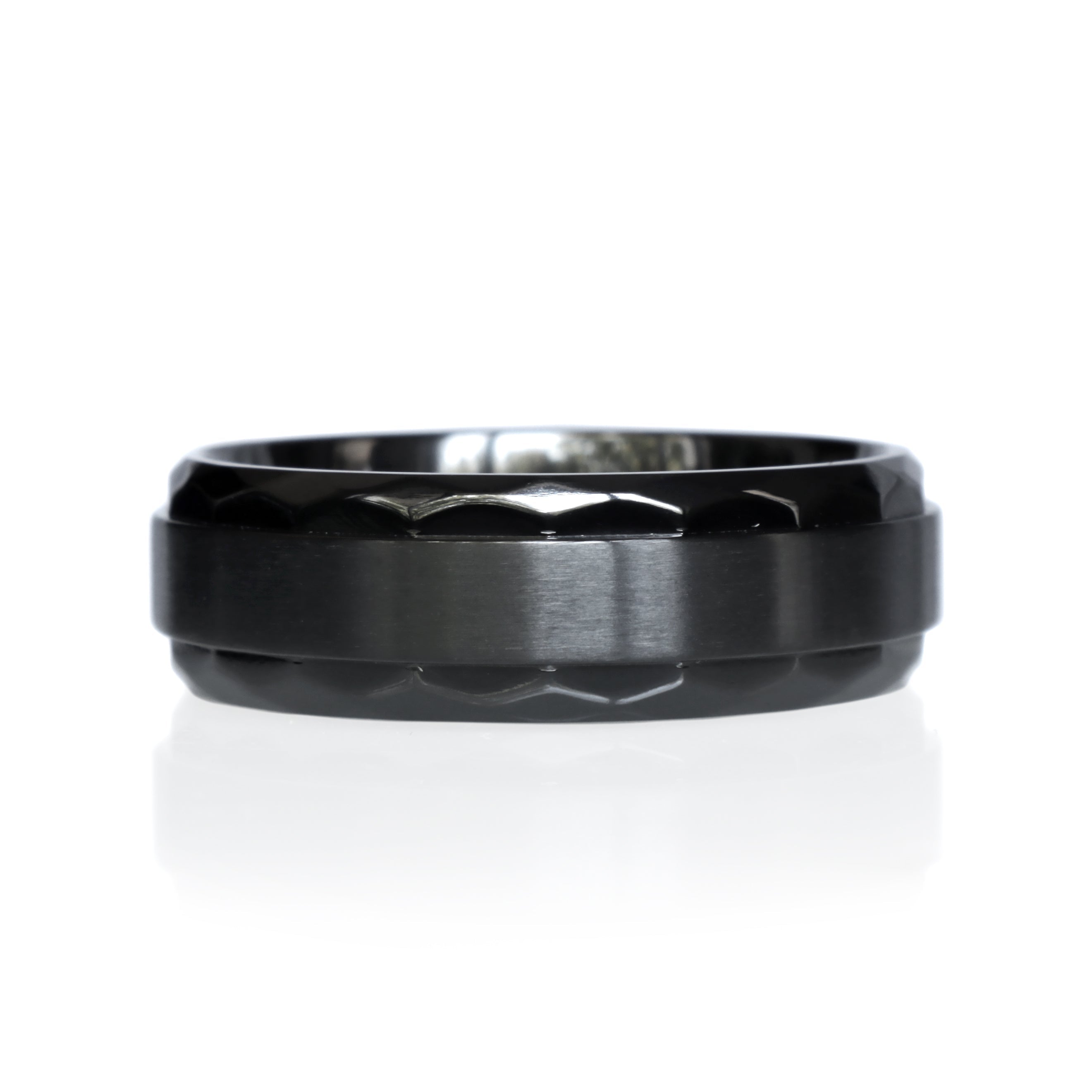 A product image of an 8mm wide ring against a plain white background. The ring is crafted from black zirconium, featuring a geometric pattern around the edges. A smooth, brushed black zirconium band runs horizontally across the center. The lighting highlights the intricate geometric details and the contrasting textures of the brushed center and patterned edges.