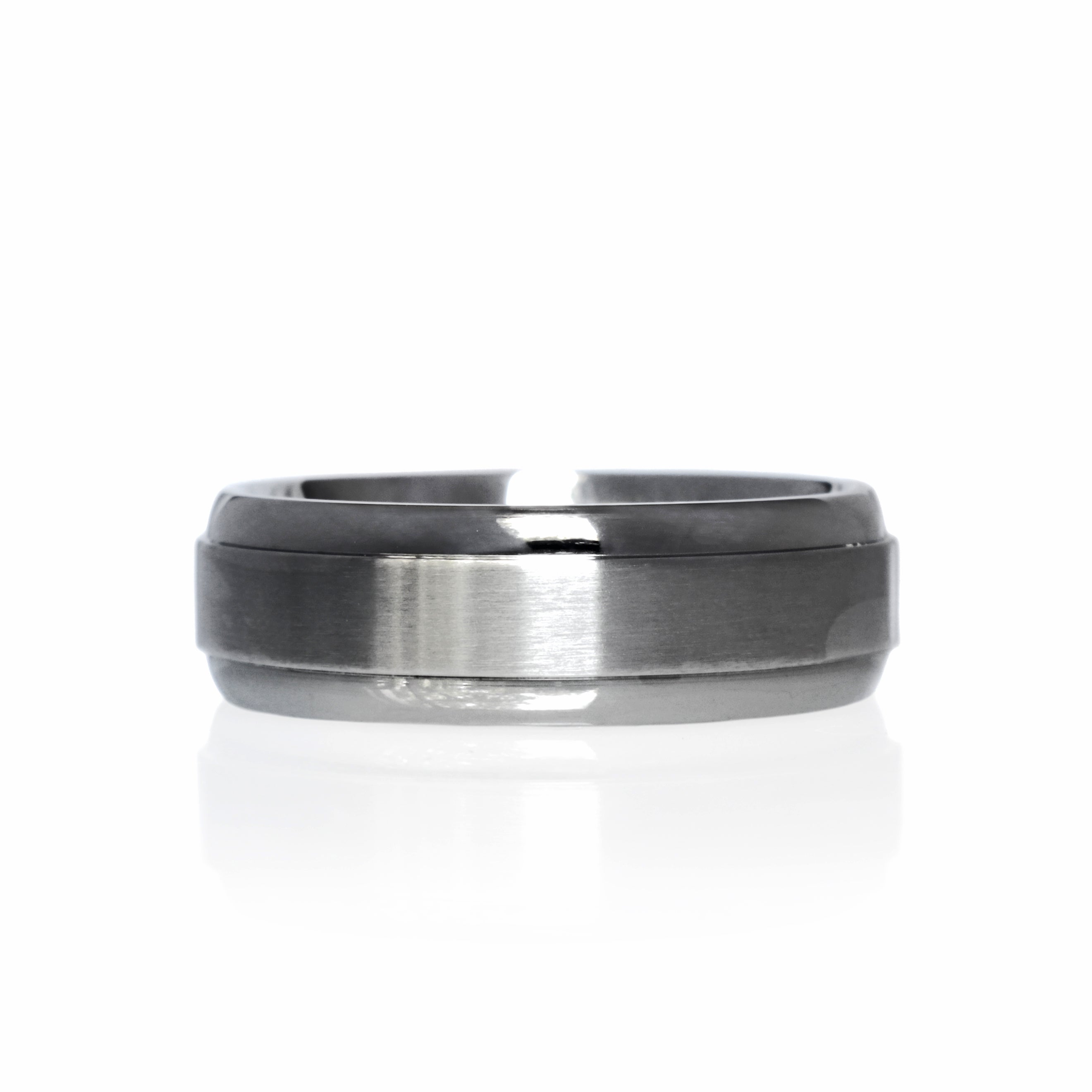 A product image of a 7mm wide ring against a plain white background. The ring is crafted from titanium with a brushed finish across the center band. The edges of the ring are polished, providing a subtle contrast to the brushed center. The lighting highlights the texture of the brushed titanium in the center and the reflective shine of the polished edges.