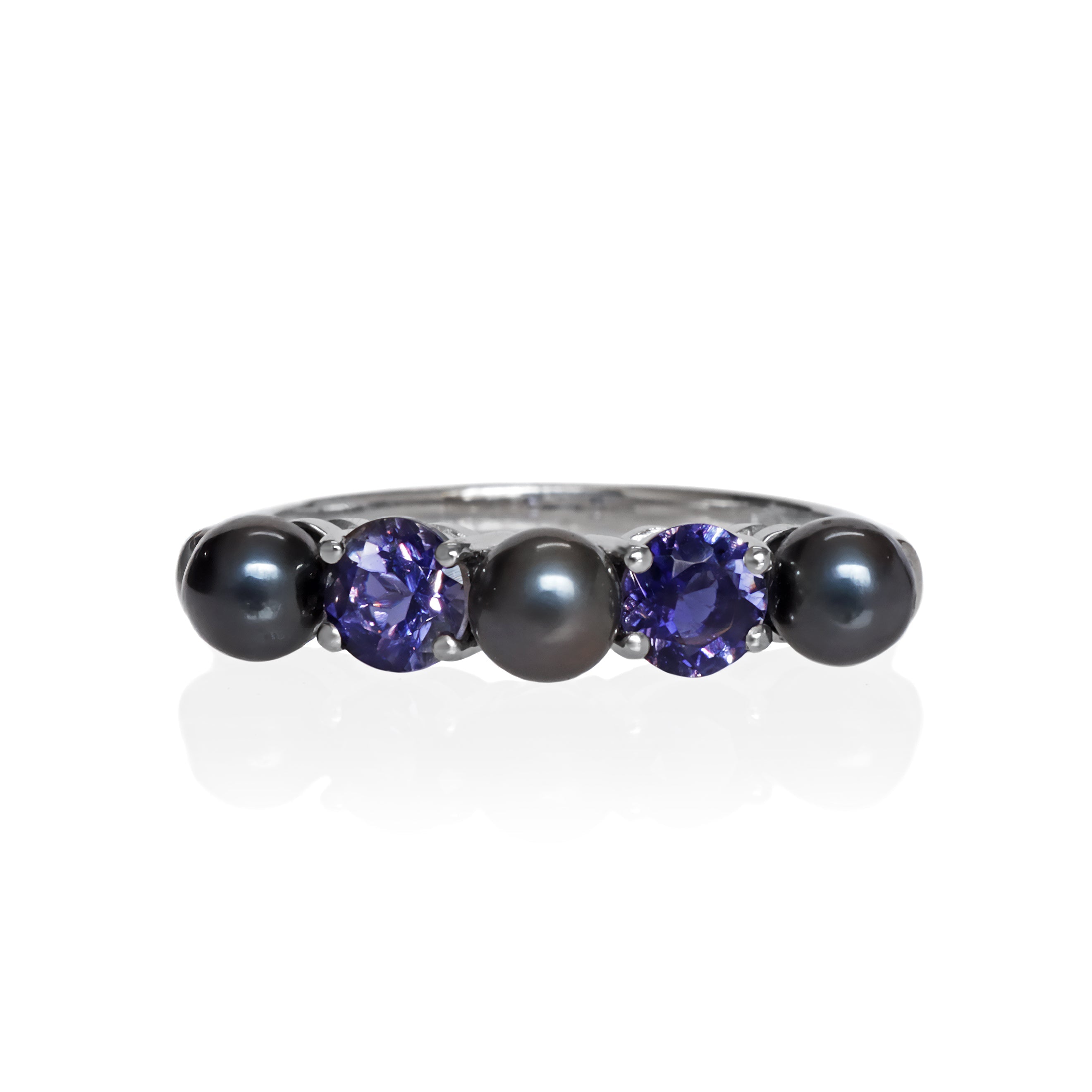 This product image shows a natural black freshwater pearl and iolite eternity ring set in solid 9 karat white gold. The ring is made up of 3 round deep grey / black pearls of 4.5mm in diameter, two on the outer edges of the eternity design and one in the centre. Between each pearl sits a midnight blue round-cut iolite jewel of similar sizing.