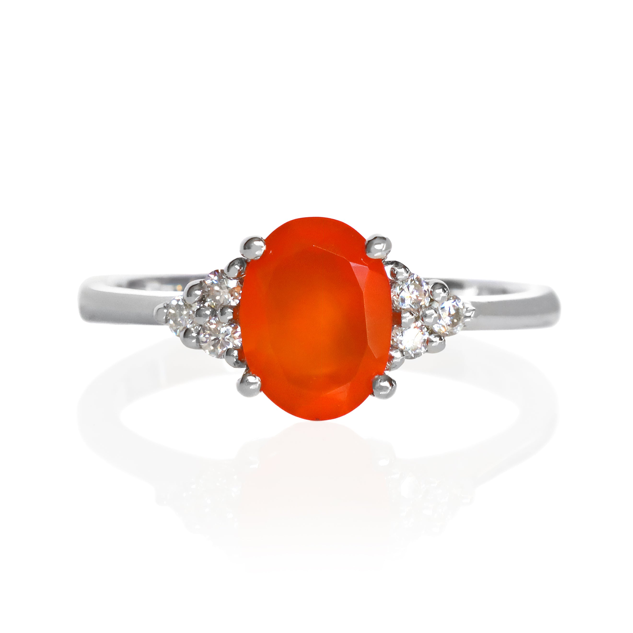A product photo of a 925 sterling silver carnelian and moissanite trio ring sitting on a white background. The oval-cut, naturally-opaque fiery orange gemstone stands in stark contrast to the clusters of three classic white moissanite stones on either side.