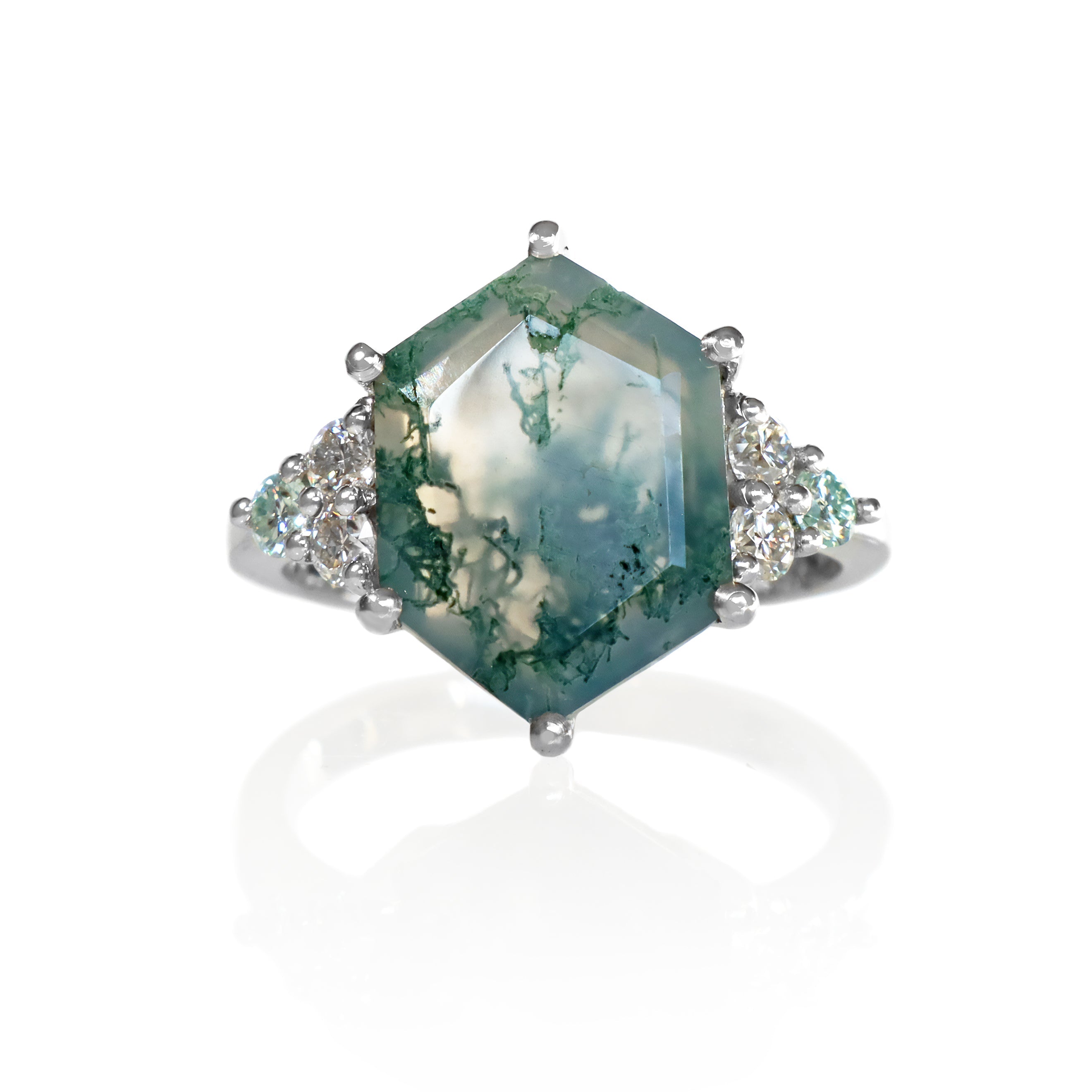 A product photo of a statement moissanite and moss agate engagement ring in solid 925 sterling silver sitting on a white background. The band is smooth and rounded. The impressively large 14x10mm Hexagonal Moss Agate gemstone is embraced on either side by a delicate trio of bright white moissanite gems.