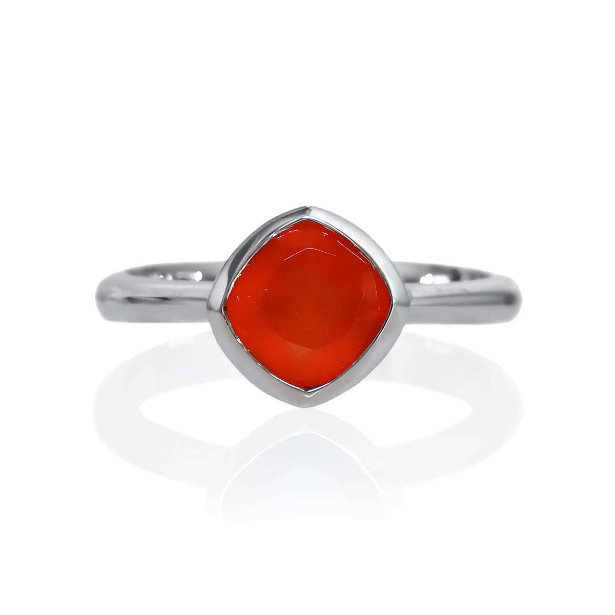 A product photo of a silver ring with a bezel-set carnelian centre stone sitting on a white background. The silver band is simple and smooth, connecting on either side of a diagonally-oriented squared-cushion carnelian stone surrounded by a solid frame of silver.
