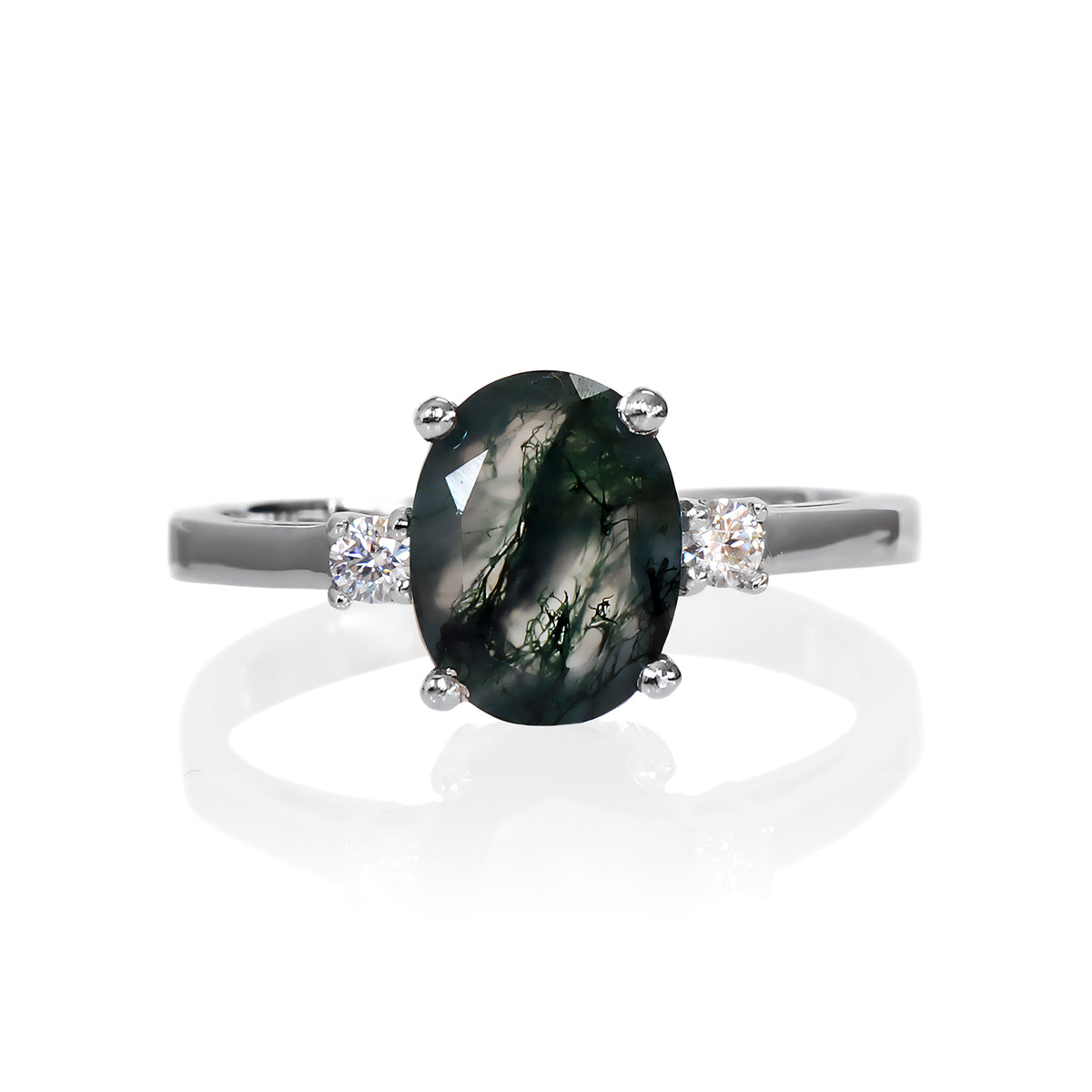 A product photo of an elegant sterling silver ring with a stunning trio of moss agate and moissanites sitting against a white background. The largest of the stones sits in the centre, an oval moss agate - hugged by two smaller circular white moissanites on either side.