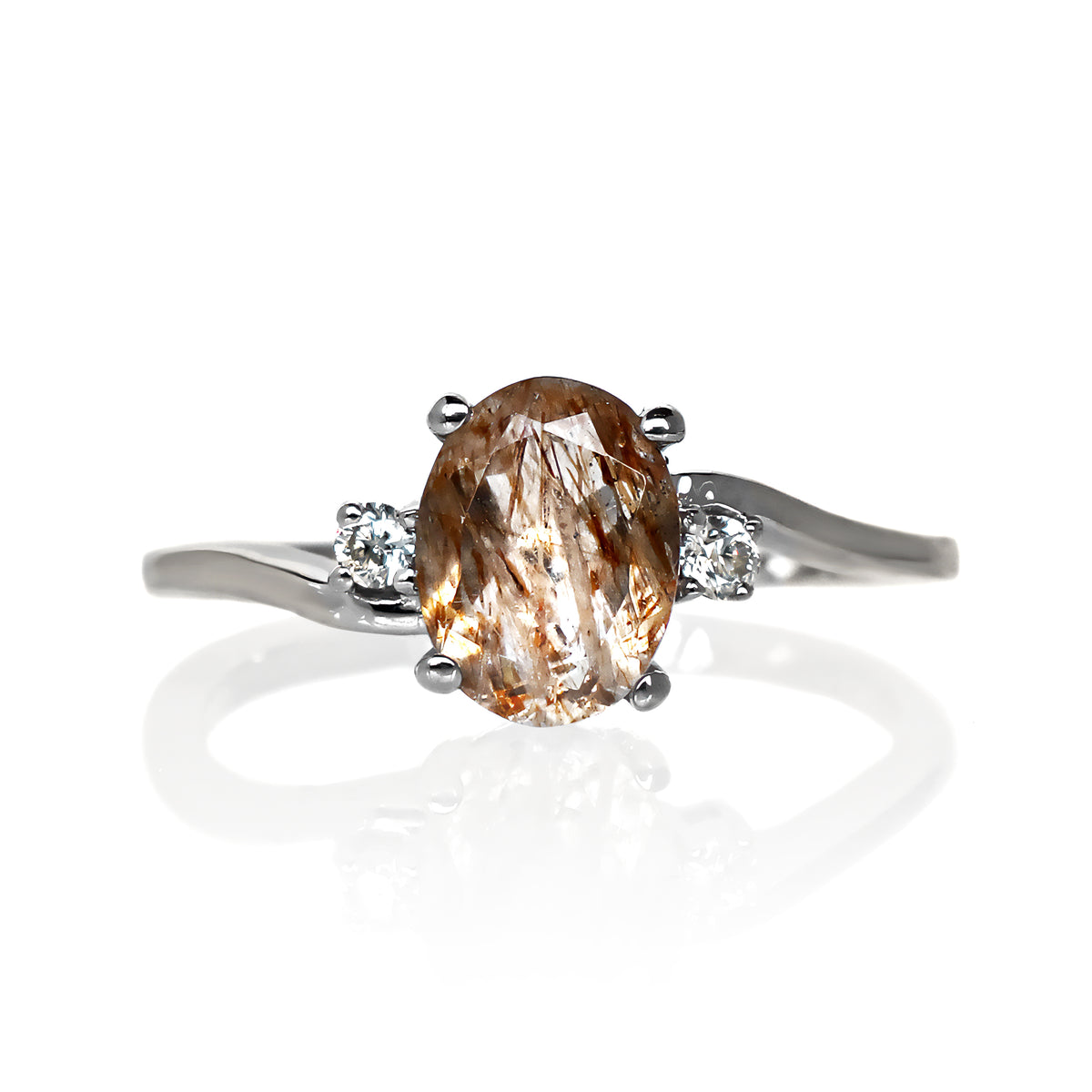 A product photo of a silver copper rutilated quartz and moissanite trio ring sitting on a white background. The oval, naturally-included copper rutilated quartz gemstone stands in stark contrast to the singular white moissanite stones on either side.