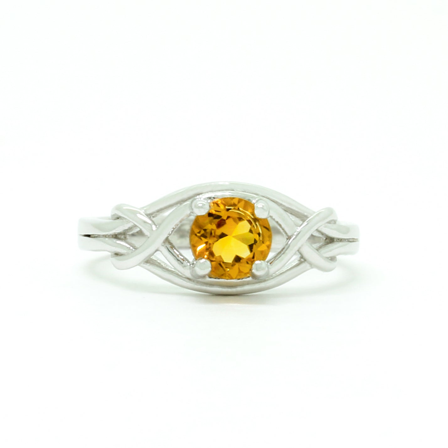 A product photo of an ornate silver ring with a circle-cut citrine centre stone sitting on a white background. The back of the silver band is simple and smooth, before splitting into four serpentine tendrils on either side that delicately coil around one another before meeting on either side of the circle-cut centre stone, which is held in place by four small silver claws. The citrine jewel is almost honey-coloured, reflecting a bright orangey yellow colour across its multi-faceted surface.