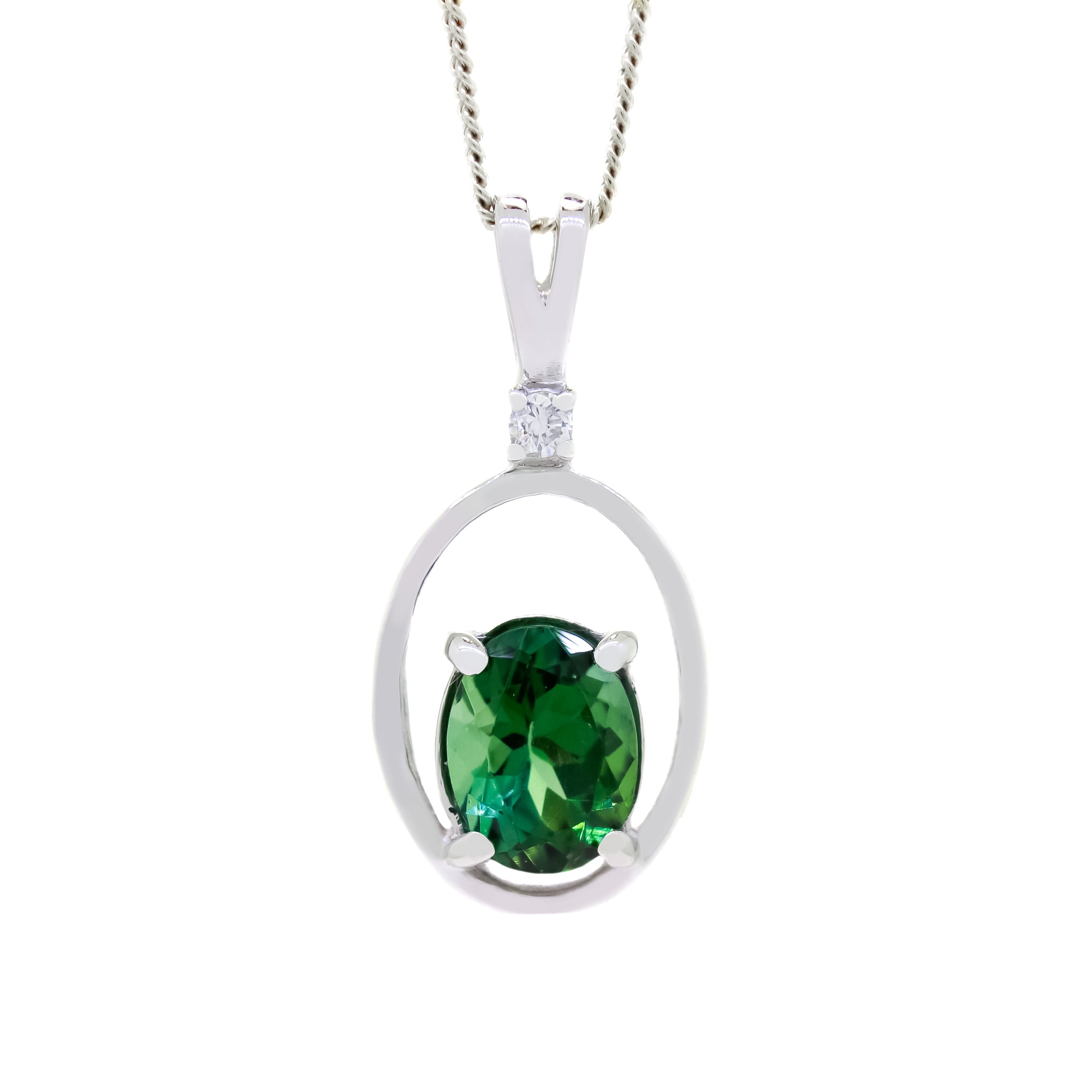 A product photo of a white gold pendant with an oval-cut green tourmaline centre stone suspended by a chain against a white background. The oval stone is oriented vertically, and rests at the bottom of a silver frame in the shape of a larger oval. The jewel reflects a cool forest green colour across its multi-faceted surface.