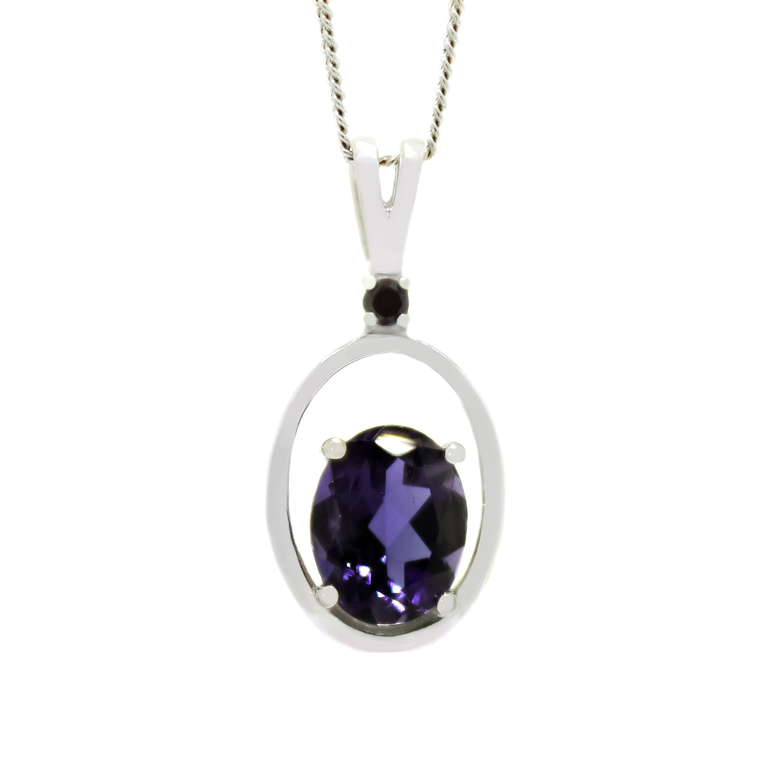 A product photo of a solid 9 karat white gold pendant with an oval-cut midnight blue iolite centre stone suspended by a chain against a white background. The oval stone is oriented vertically, and rests at the bottom of a golden frame in the shape of a larger oval. The jewel reflects a cool, deep indigo colour across its multi-faceted surface. The dark blue colour could make it a good sapphire or tanzanite alternative.