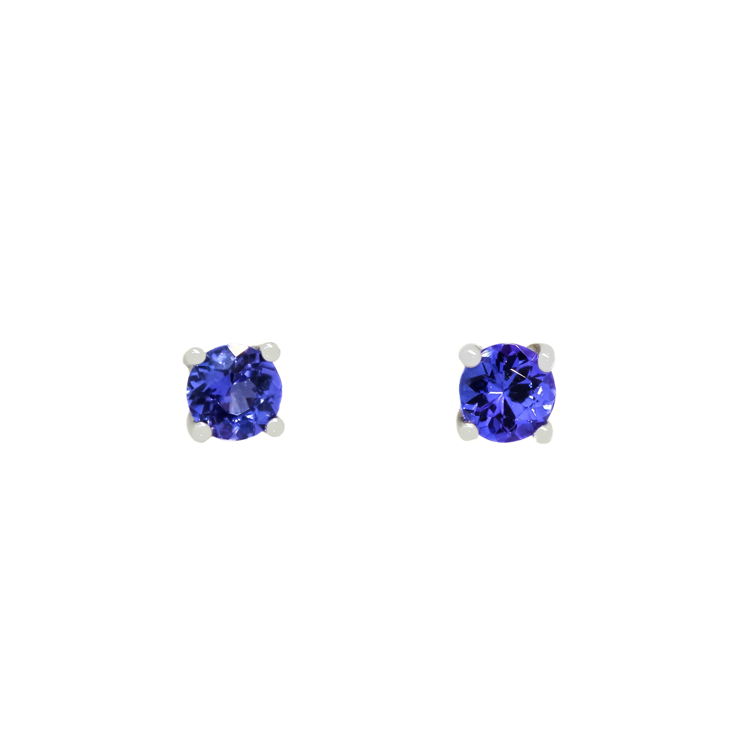 A product photo of two white gold stud earrings sitting on a white background. Held in place by 4 silver claws each are two dazzling round-cut indigo blue tanzanite gemstones, reflecting shades of cool violet from their many edges.