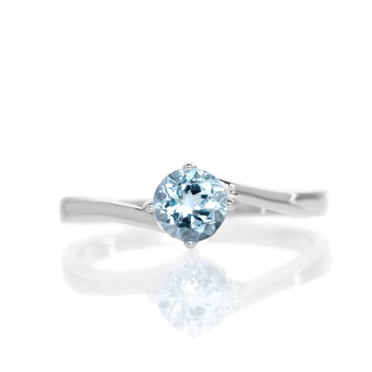 A product photo of a curved-band silver solitaire ring with a pale bllue aquamarine centre stone sitting on a white background.