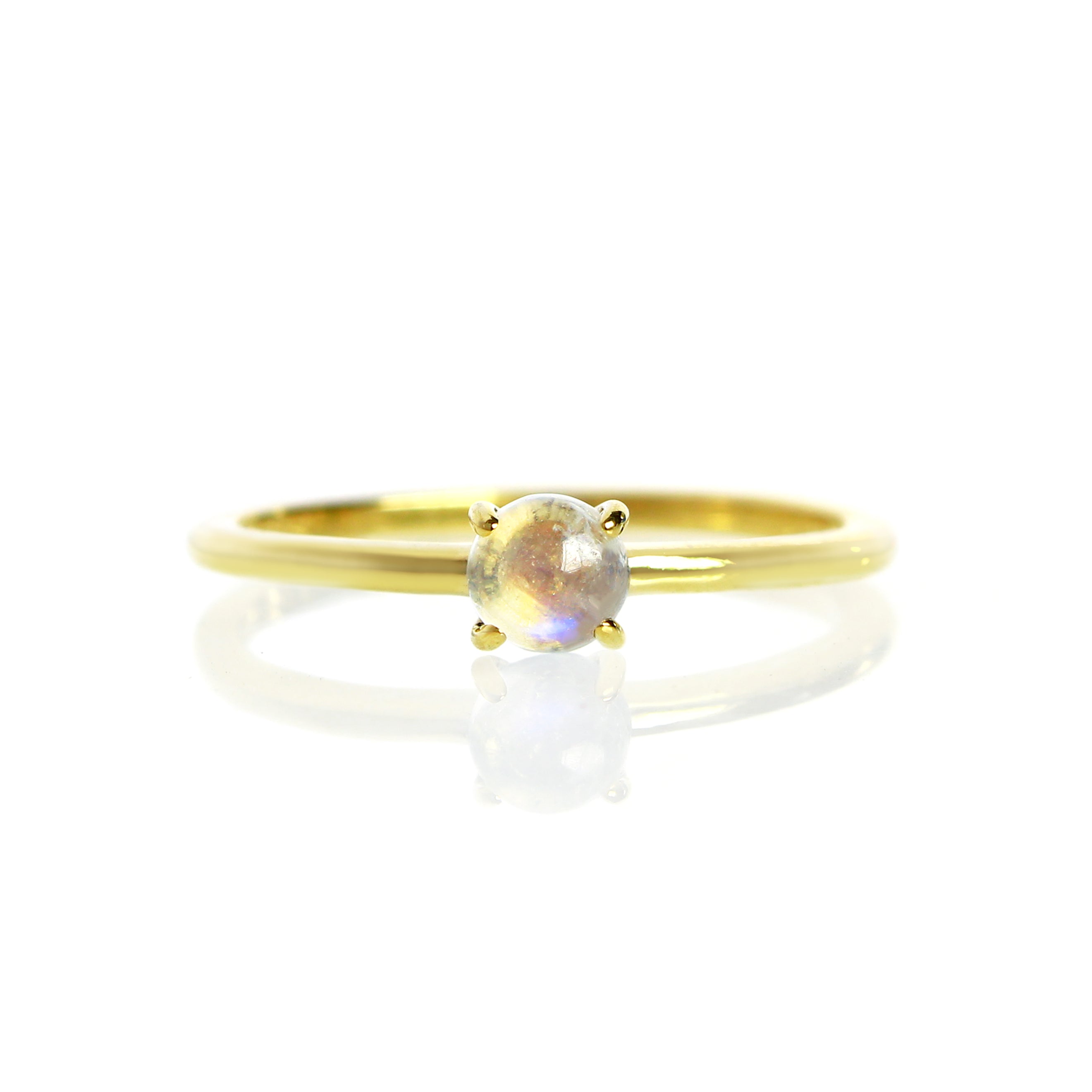 A product photo of a 4mm cabochon moonstone solitaire stacking ring in 9k yellow gold. The ring's band is delicately thin, and flattened horizontally. The white moonstone gem is held in place by 4 delicate golden claws.