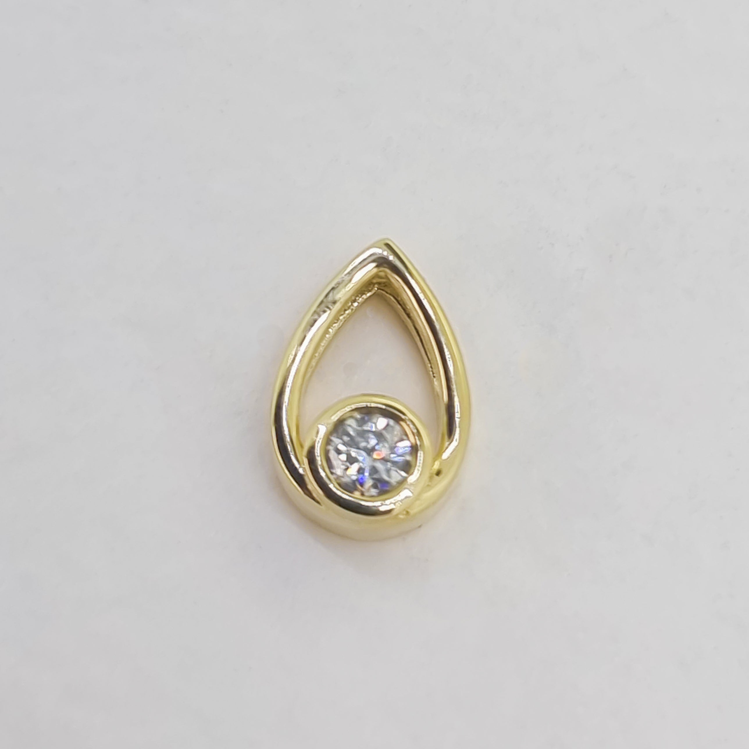 A product photo of a moissanite pendant in yellow gold sits on a clear white background. The pendant is in the shape of a small teardrop, with a petite gold-encased circle-cut moissanite gem nestled at its base. The yellow gold teardrop is smooth and unblemished.