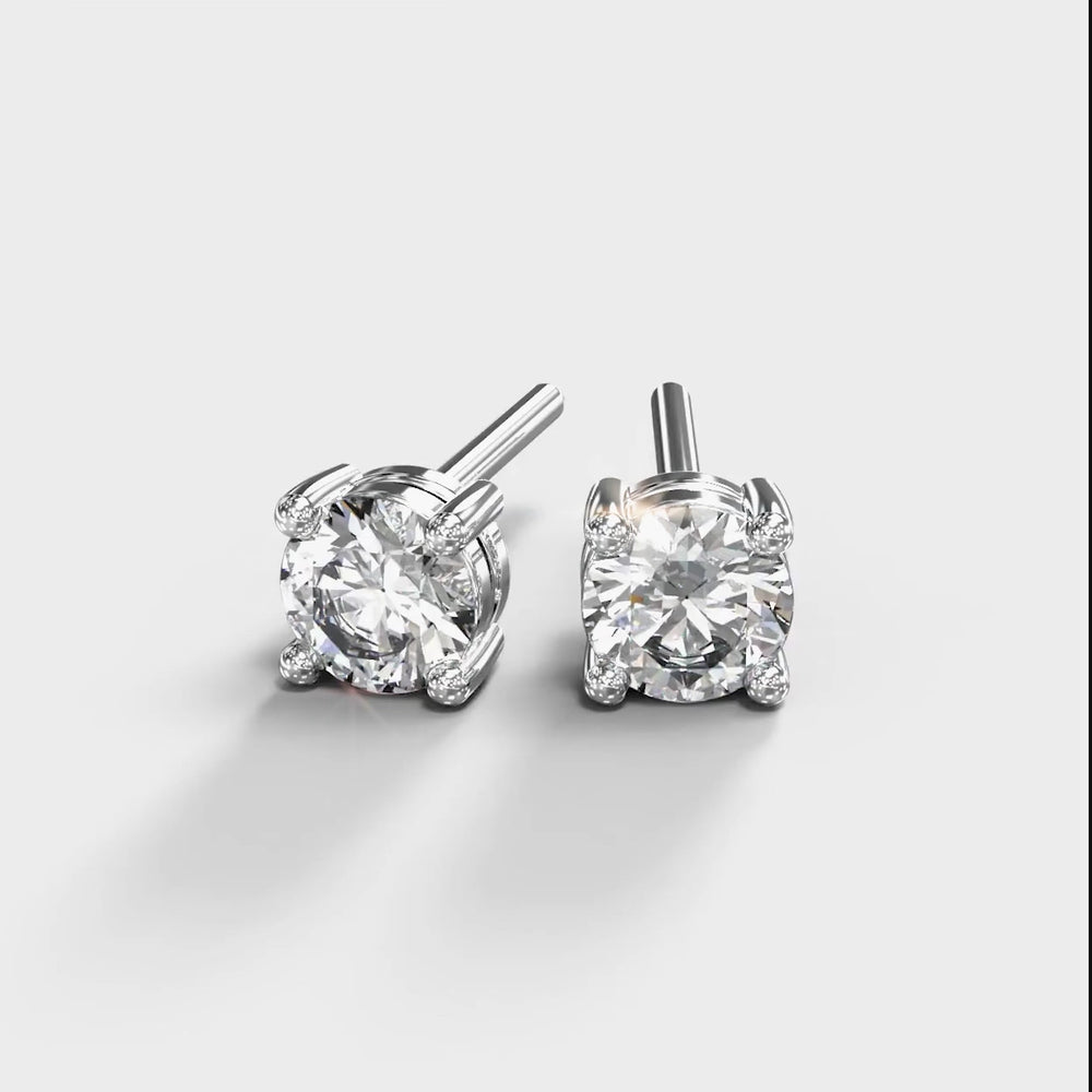 
            
                Load and play video in Gallery viewer, A product photo of a pair of 9 karat white gold lab diamond stud earrings sitting in the sun on a white textured background. The brilliant, colourless half pointer round diamonds measure 4mm across, and are held in place by a simple 4-claw setting.
            
        