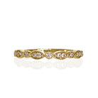 A product photo of an ornate moissanite ring in 9k yellow gold. Oval gold frames adorned with two small moissanite gems each alternate with circular gold frames adorned with singular moissanite gems and make up the ring for about half of its length before smoothing out into a simple rounded yellow gold band.
