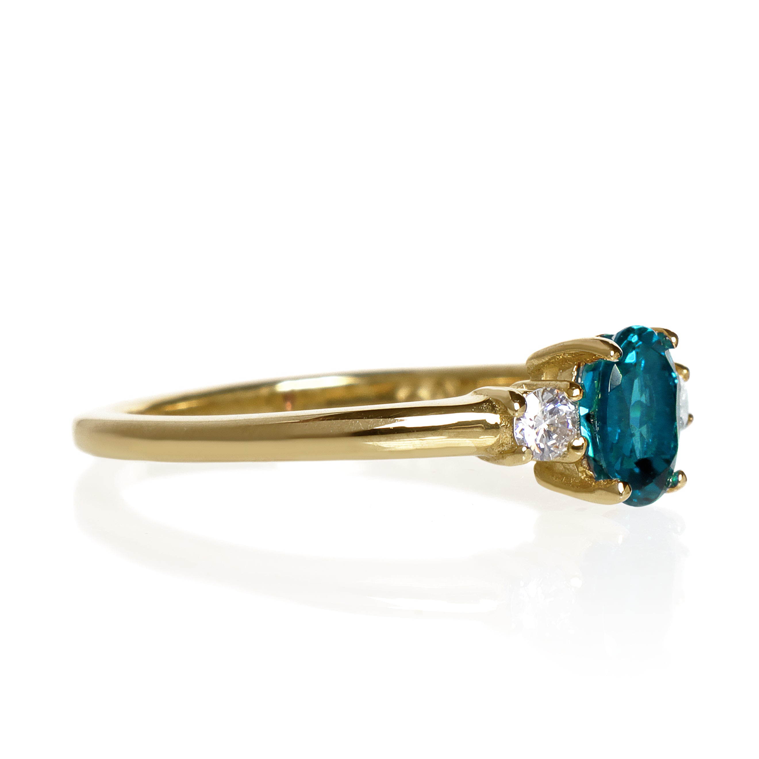 A product photo of a yellow gold london blue topaz ring sitting against a white background. The golden band is plain and smooth, and the centre upright octagonal topaz stone is framed by a single white diamond on either side.