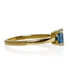 A product photo of a yellow gold london blue topaz ring sitting against a white background. The golden band is plain and smooth, contrasted by the large square cushion-cut ocean blue stone in the centre.