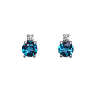 A product photo of a pair of white gold london blue topaz earrings sitting against a white background. The simple circle-cut stones are complimented by a single white diamond atop each stone, encased in white gold.